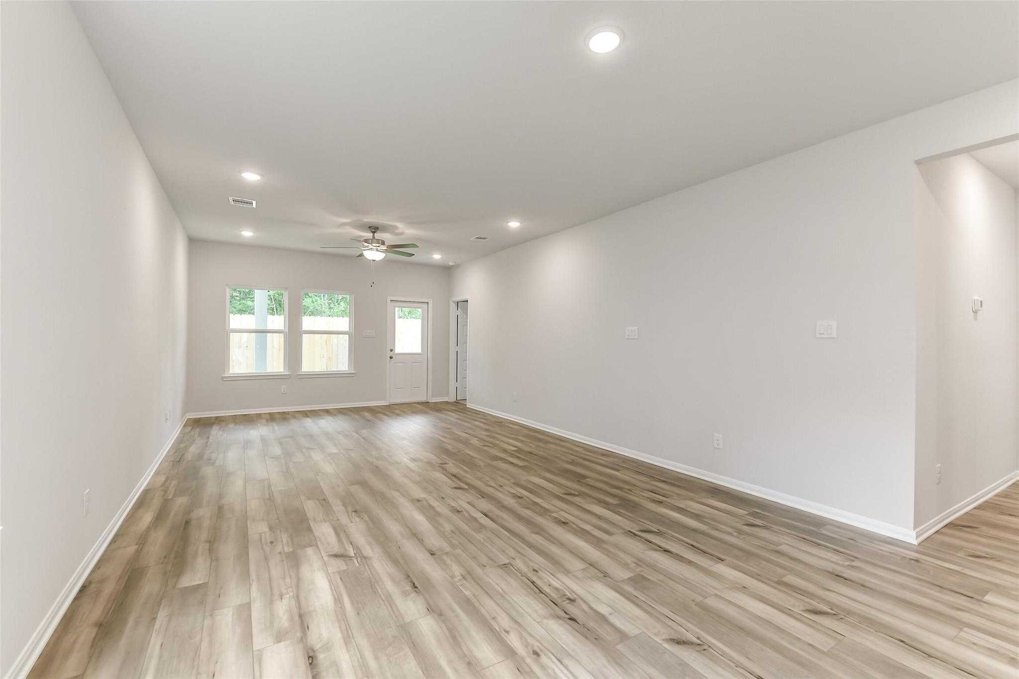 Spacious living room with light hardwood floors, ceiling fan, and large windows in Davidson Homes Sabine F, Conroe TX