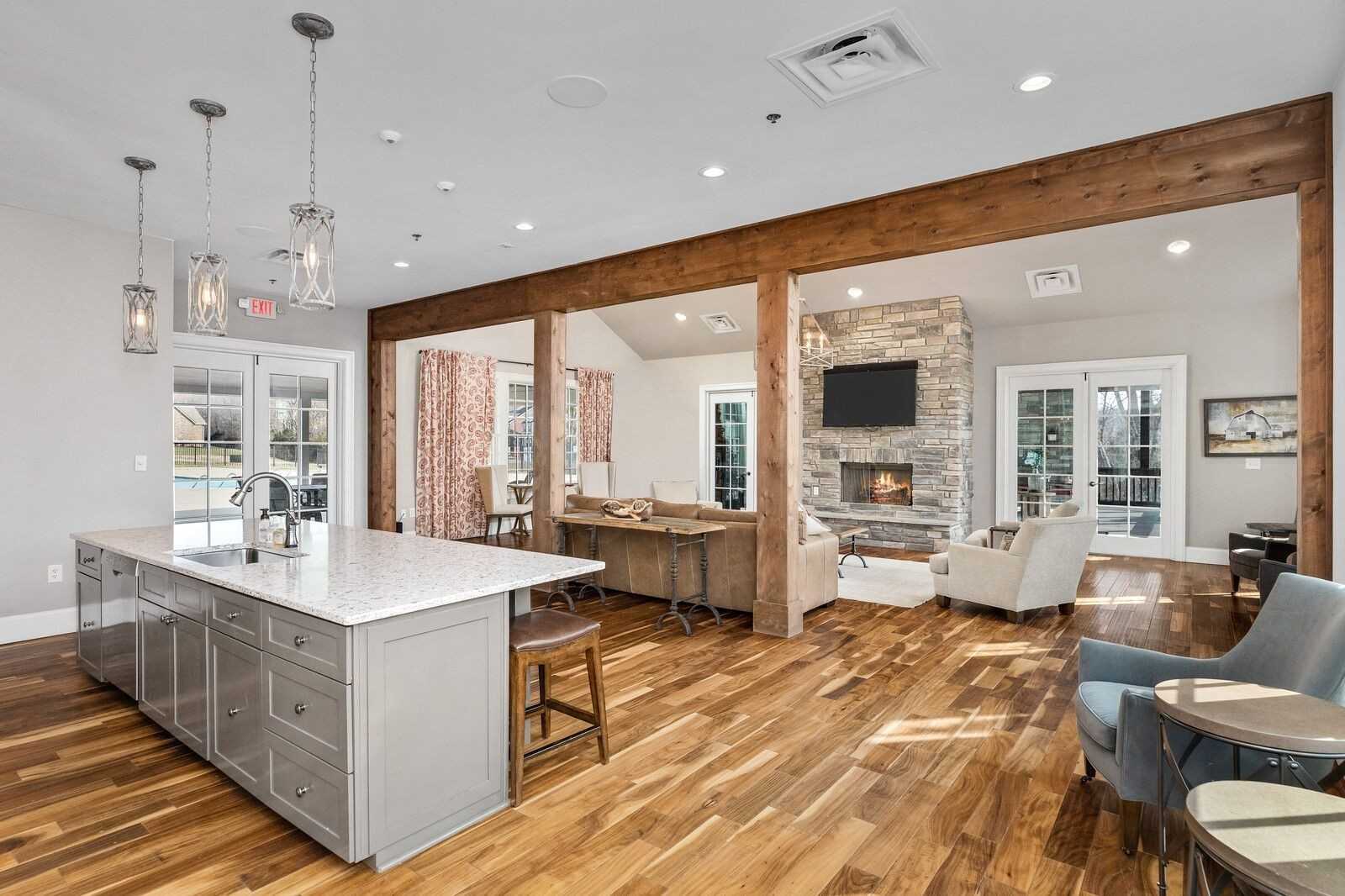 Spacious open-concept great room with wooden beams, stone gas fireplace, white quartz island, cozy seating, and hardwood floors in Davidson Homes The Ridgeport, Gallatin, TN