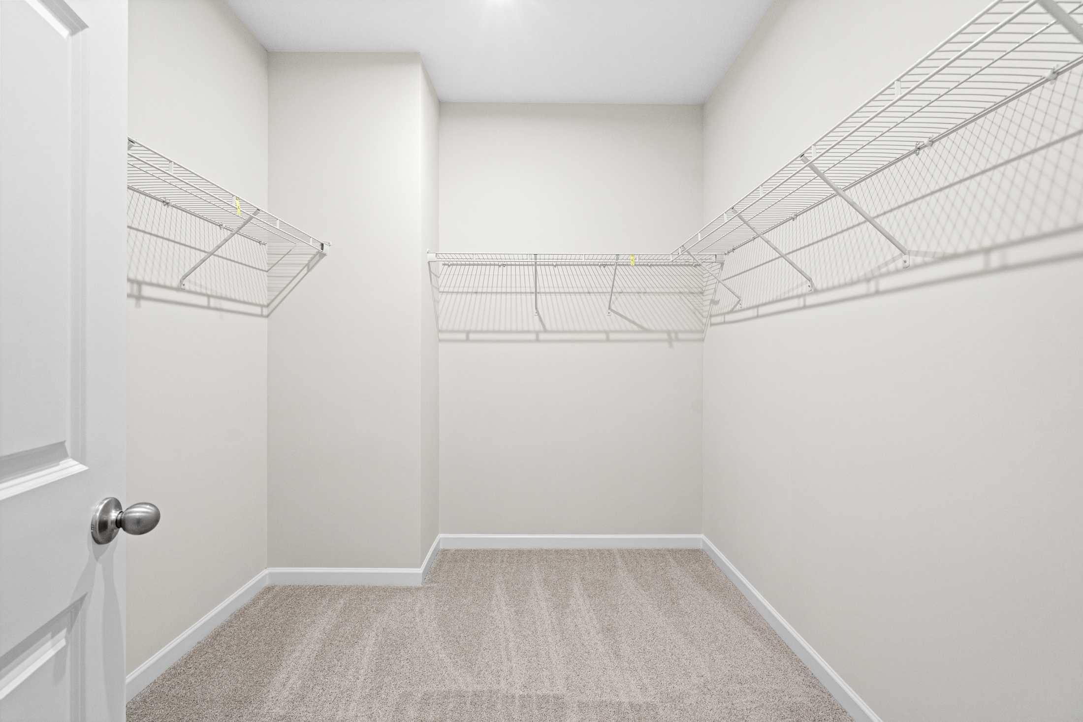 Spacious walk-in closet in The Glenwood A master suite featuring white wire shelving and beige carpet