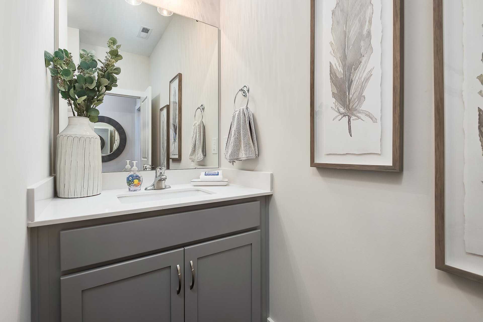 Modern master bathroom in The Everett home by Davidson Homes with gray vanity, round mirror, eucalyptus accents, and feather wall art