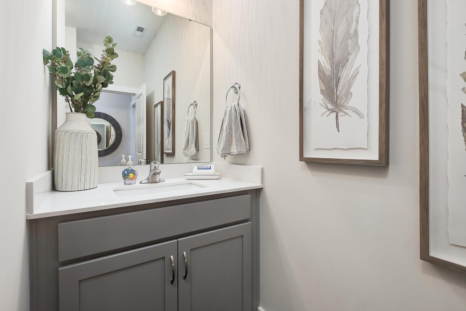 Modern powder room in The Everett with gray vanity, white sink, large mirror, eucalyptus vase, and feather art