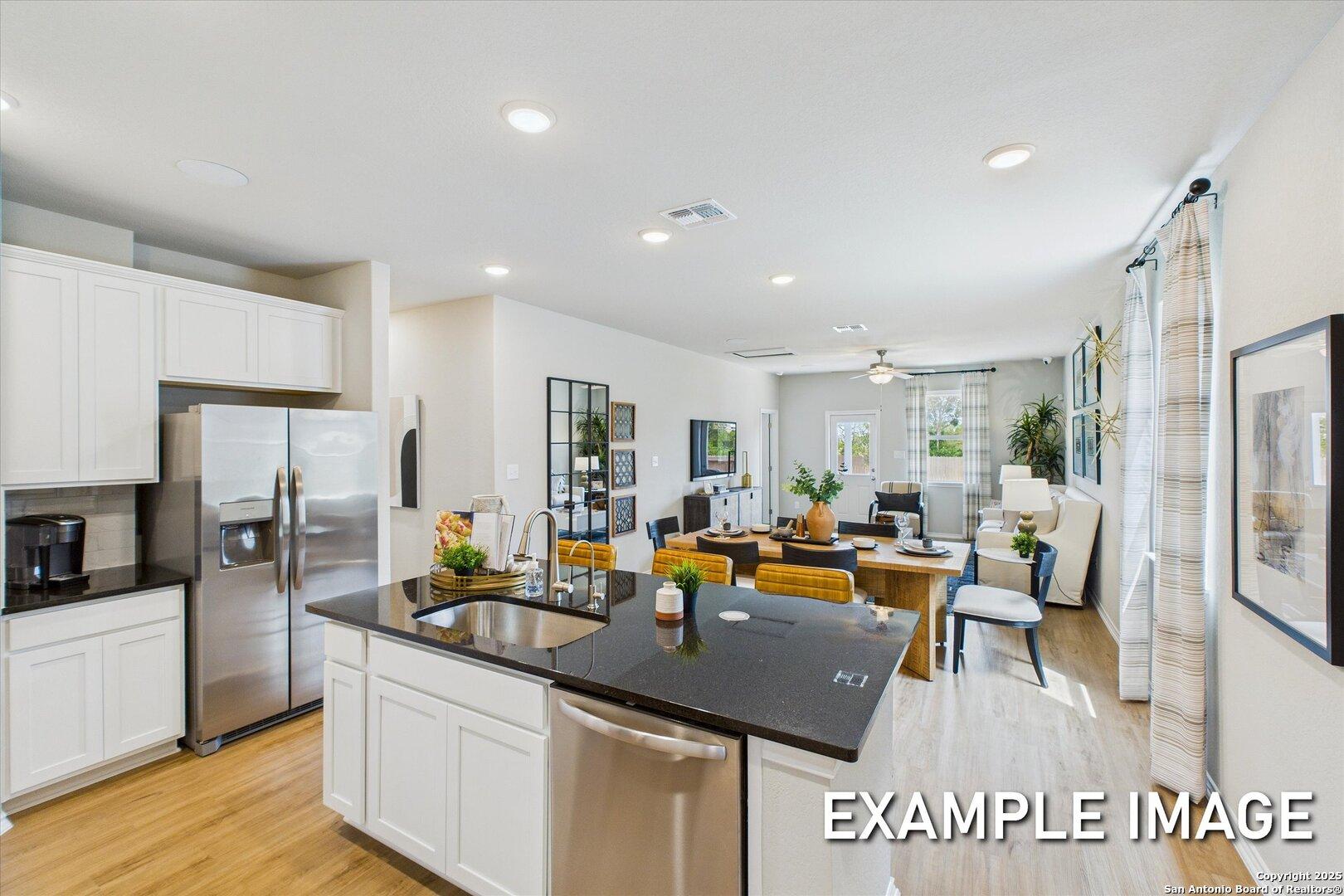 Open-concept kitchen with white cabinets, black granite island, stainless appliances, and adjacent living area in The Sabine B, San Antonio