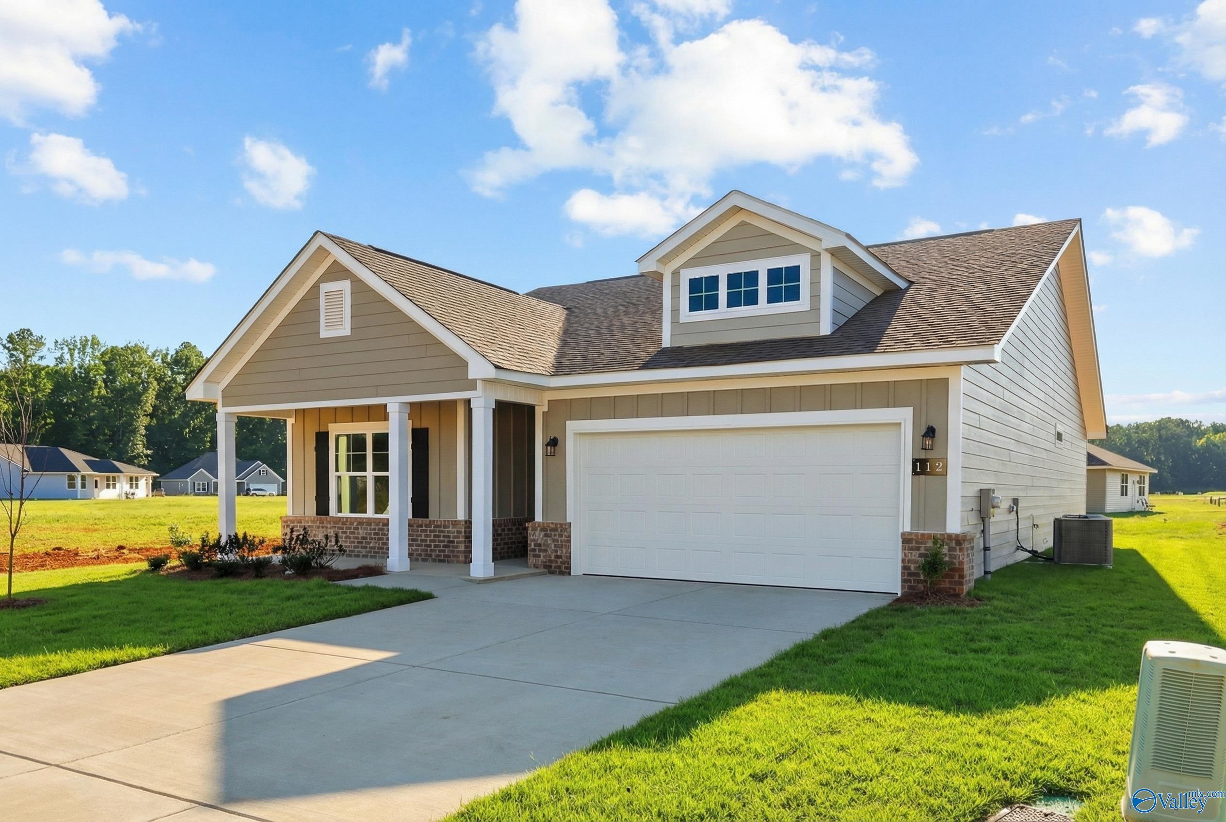 Tan single-story home with gabled roof, dormer window, covered porch, 2-car garage, and brick accents in Forest Glen, Hazel Green, Alabama