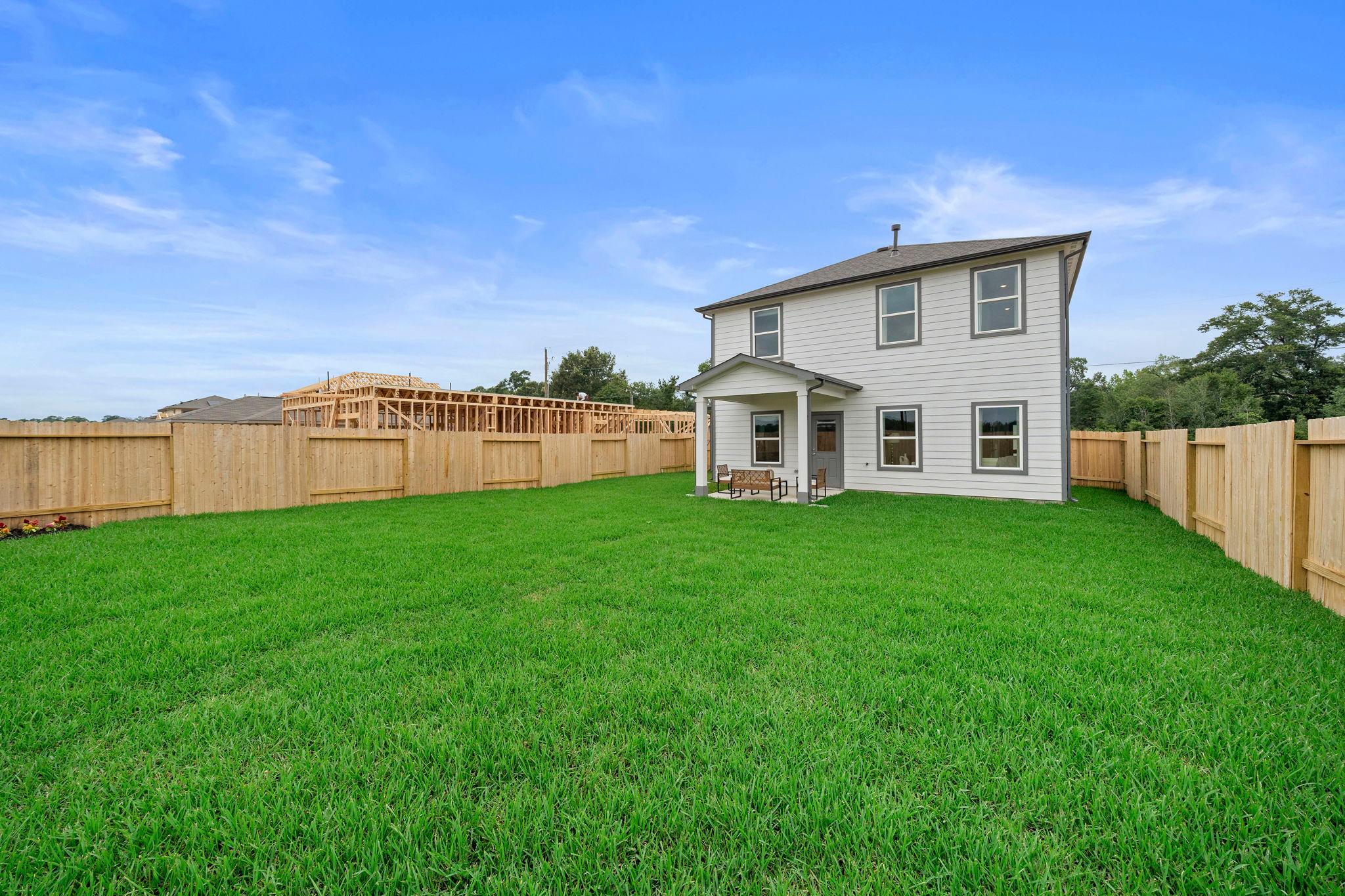 Modern white home with covered porch at Spring Branch Crossing in Conroe TX, lush green yard, wooden fence, and construction backdrop