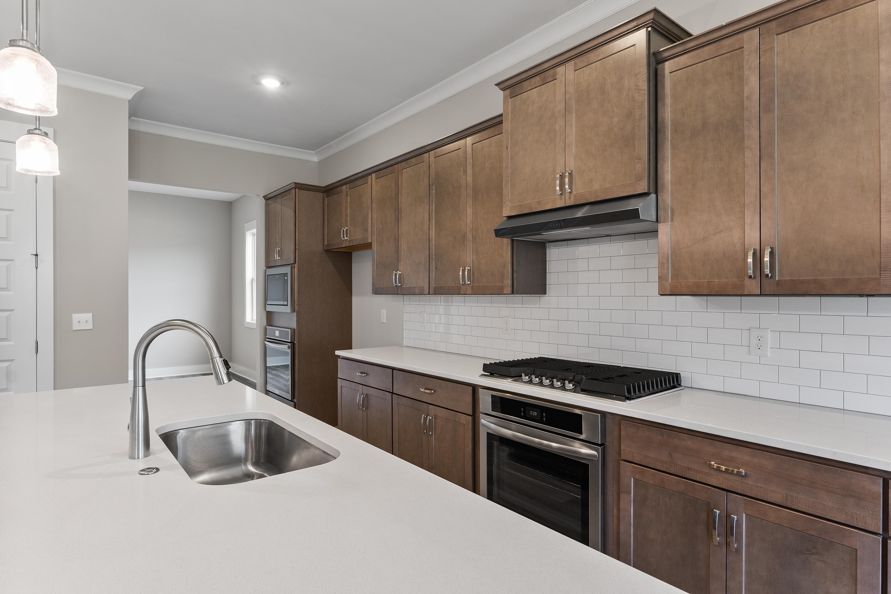 Modern kitchen in The Oxford C featuring warm shaker cabinets, white quartz island, subway tile backsplash, and stainless steel appliances