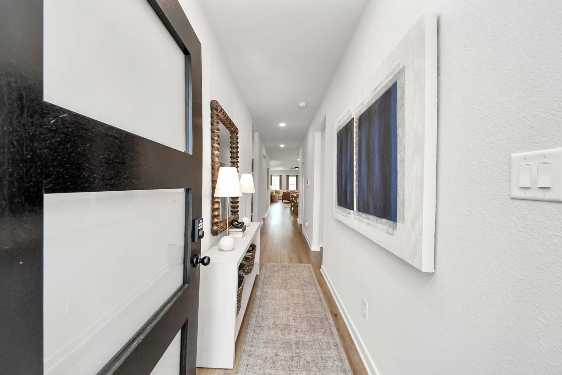 Modern entryway hallway at Enclave at Newport in Crosby, TX by Davidson Homes featuring wood flooring and wall art.