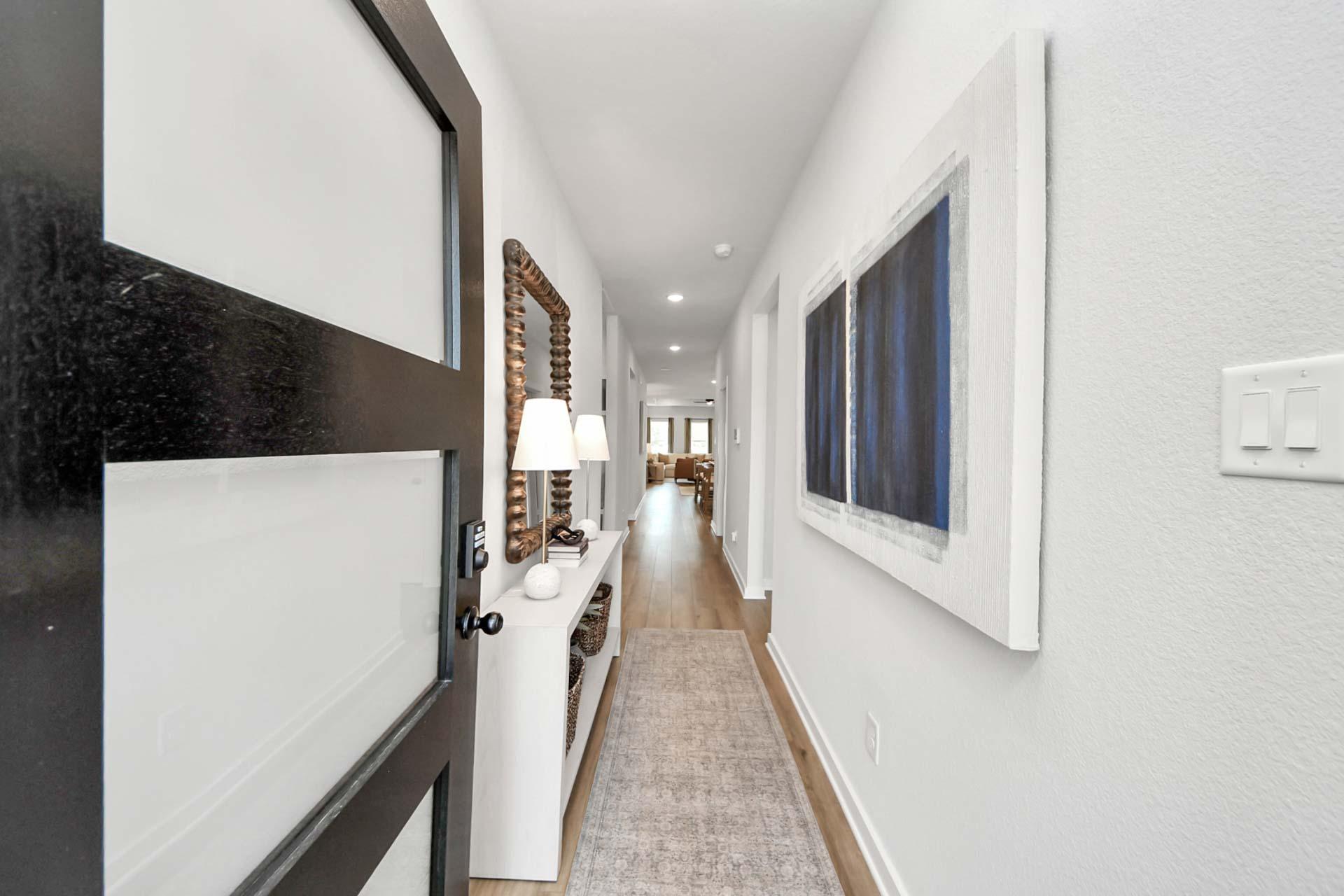Modern entryway hallway at Enclave at Newport in Crosby, TX by Davidson Homes featuring wood flooring and wall art.