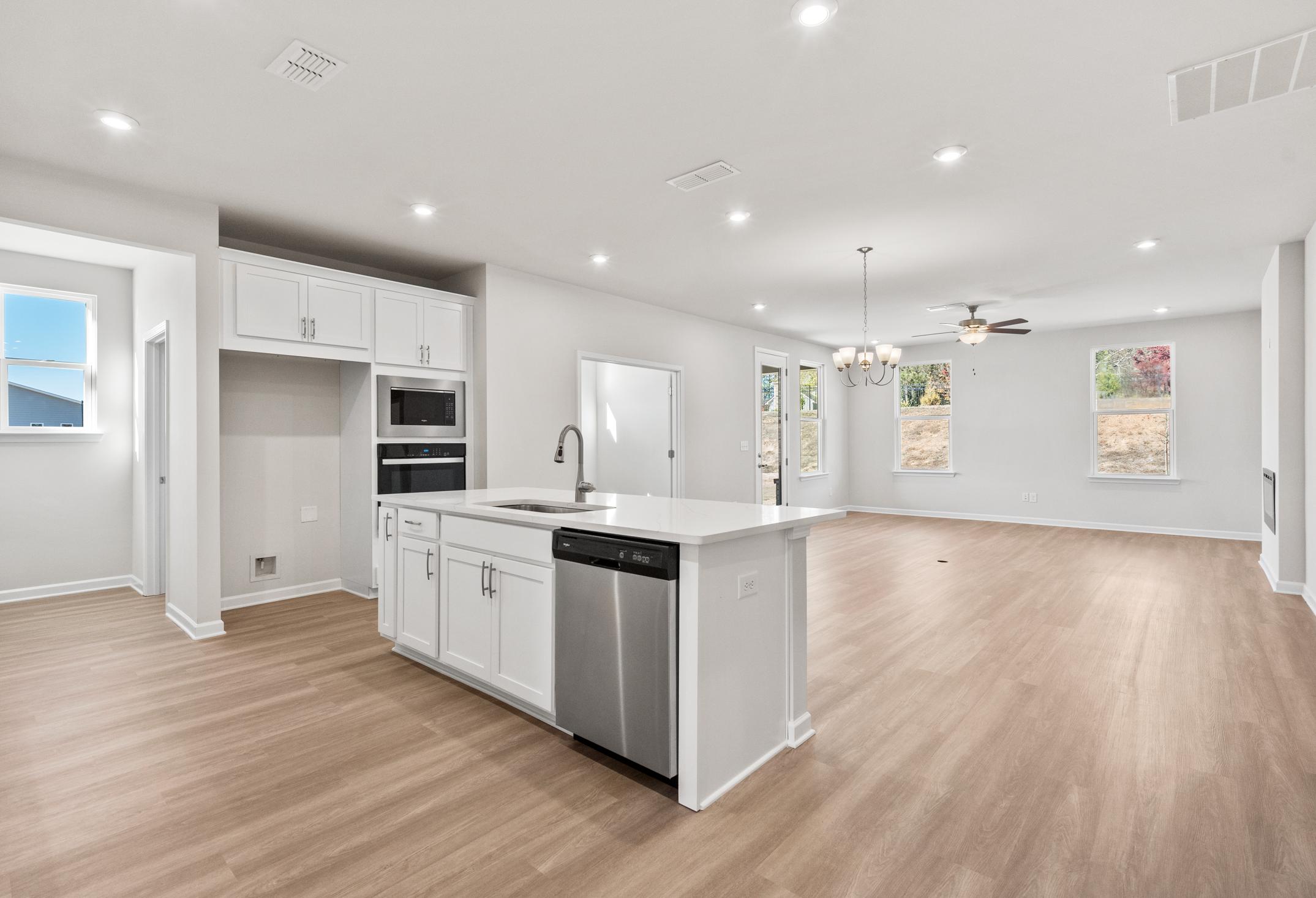Spacious open-concept kitchen in The Dawson C with white shaker cabinets, large island, stainless steel dishwasher, and hardwood floors