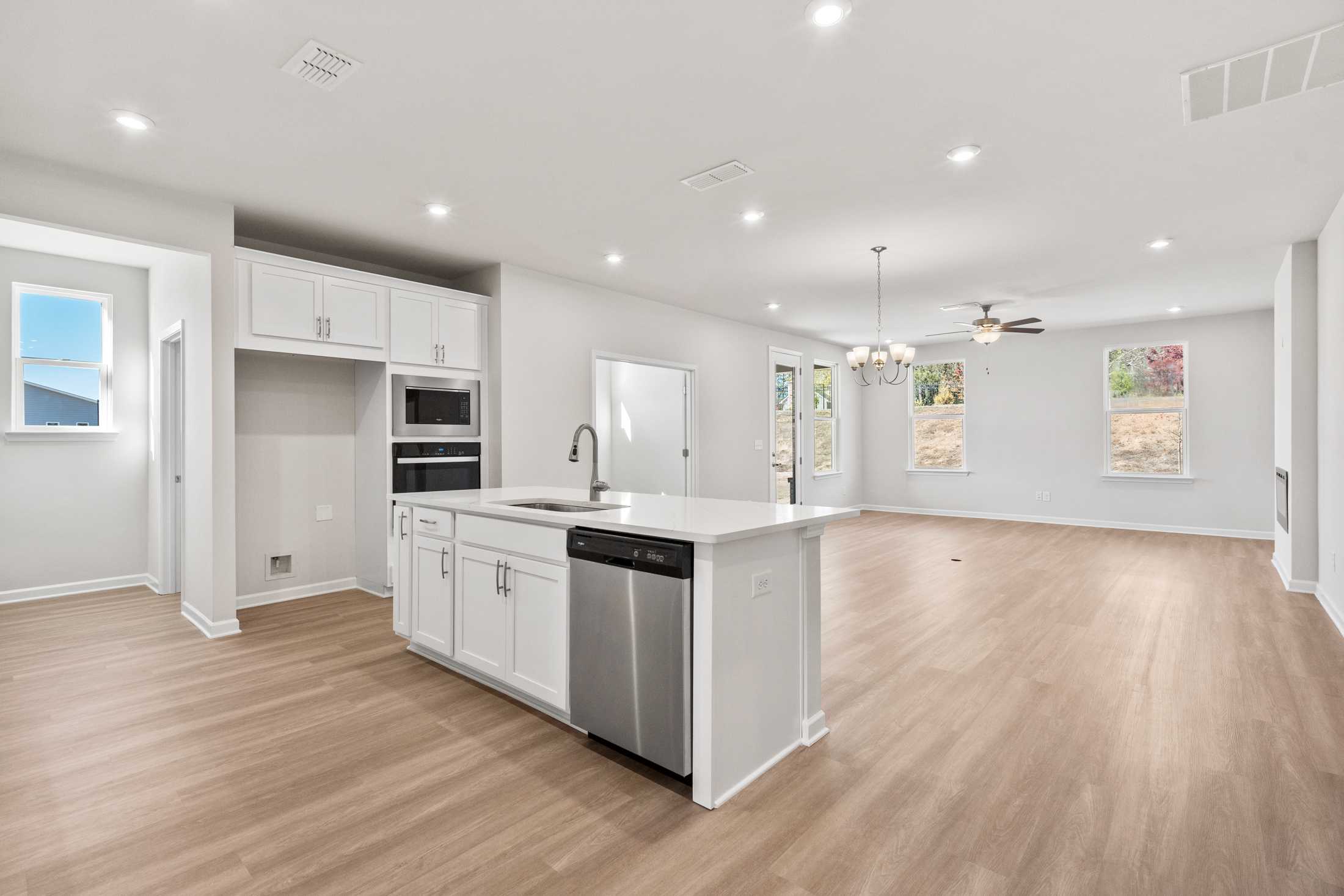 Spacious open-concept kitchen in The Dawson C with white shaker cabinets, large island, stainless steel dishwasher, and hardwood floors