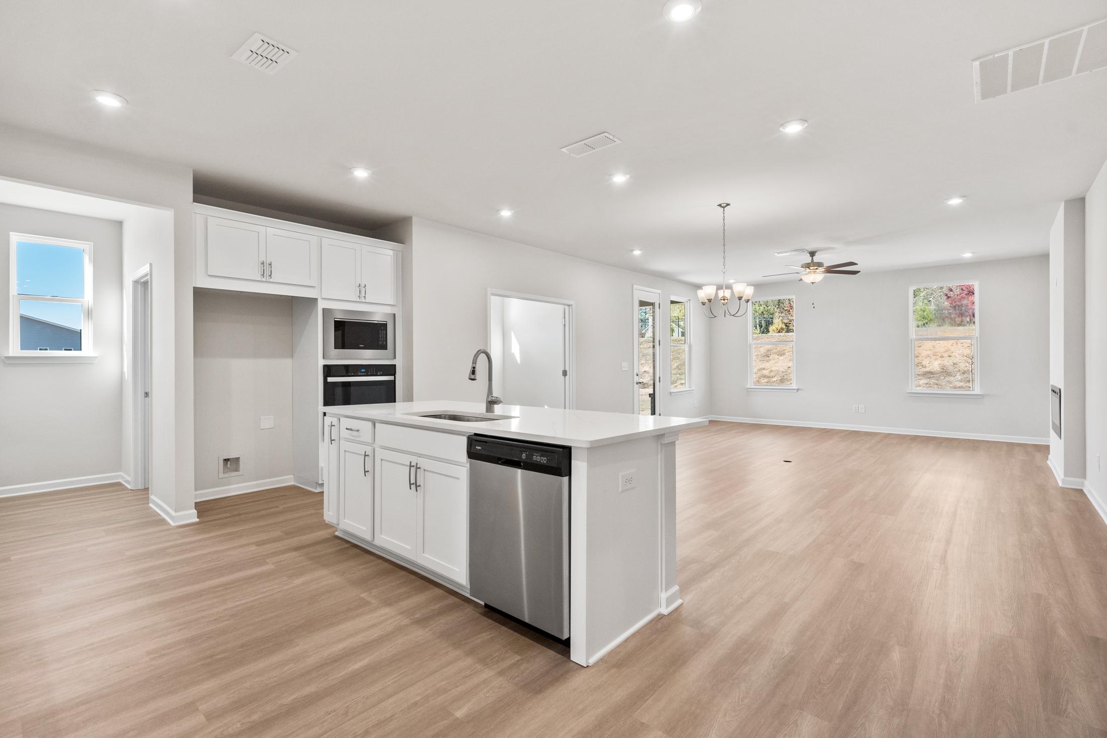 Spacious open-concept kitchen in The Dawson C with white shaker cabinets, large island, stainless steel dishwasher, and hardwood floors