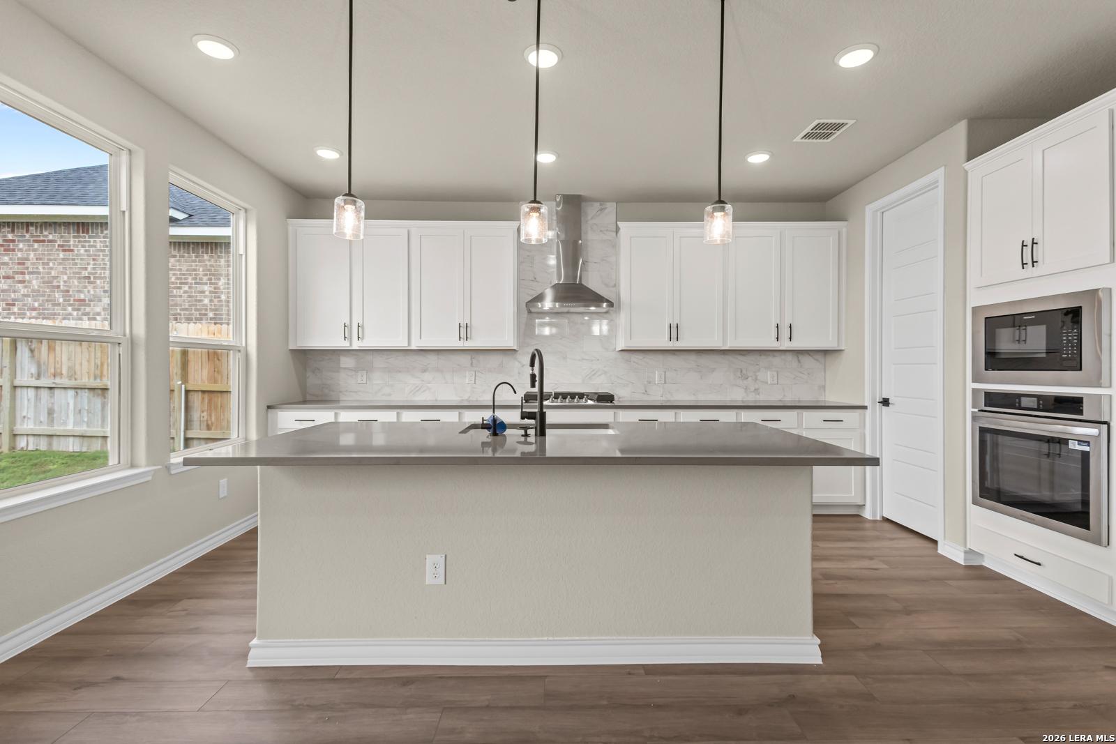 Modern kitchen with white cabinets, large island, and stainless appliances in The Danbury H, Potranco Oaks, Castroville.