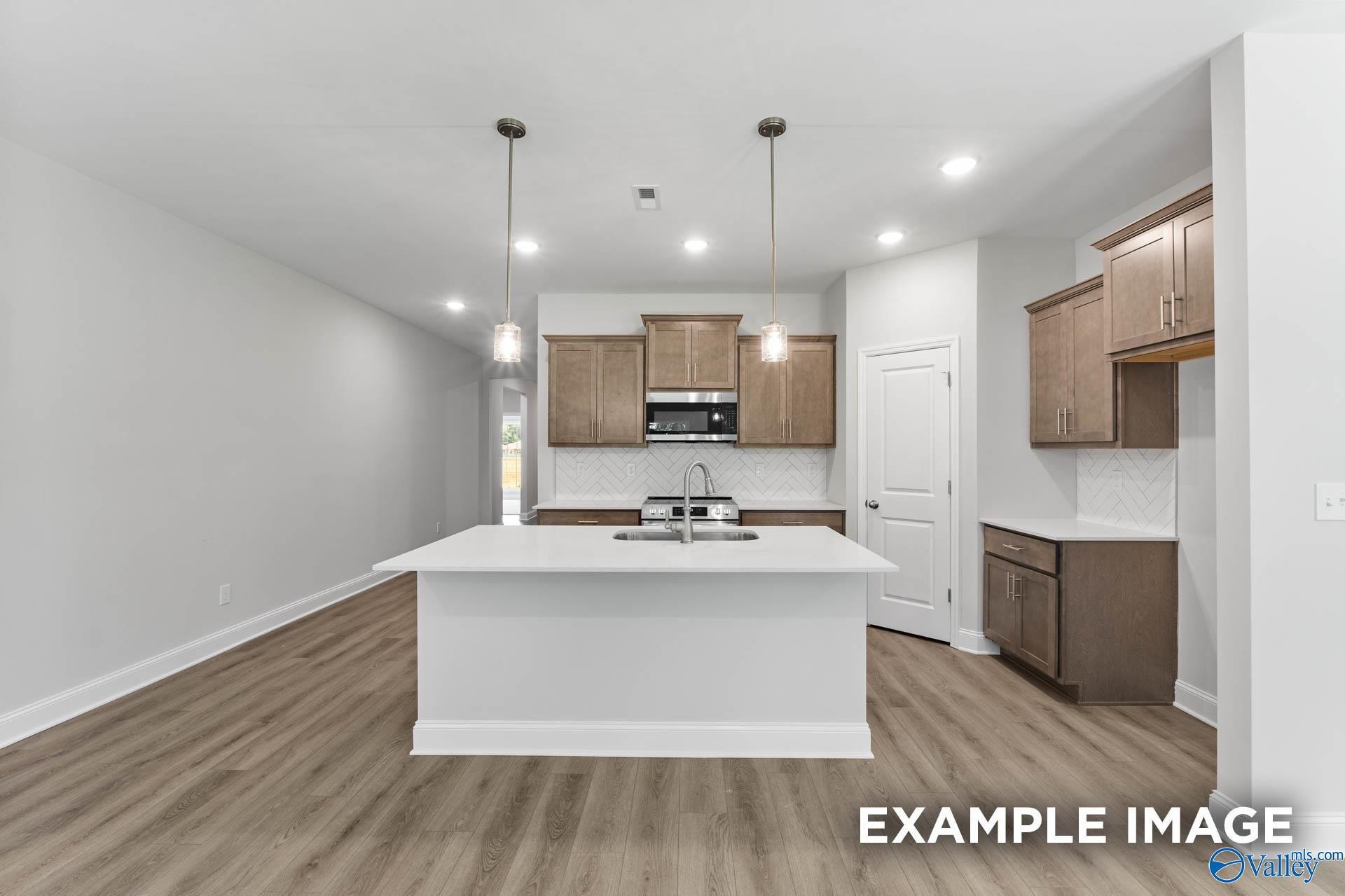 Modern kitchen with white quartz island, brown shaker cabinets, stainless appliances in The Daphne C, Arab, Alabama