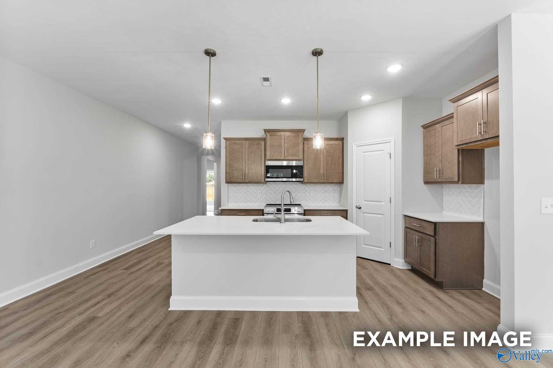 Modern kitchen with white quartz island, brown shaker cabinets, stainless appliances in The Daphne C, Arab, Alabama