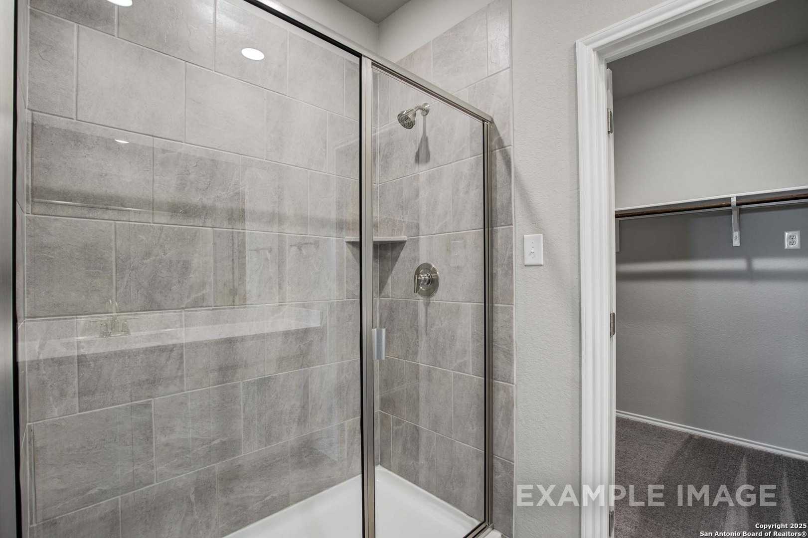Modern walk-in shower with frameless glass door, gray subway tiles, and niche in master bath of Davidson Homes The Blanco C, San Antonio