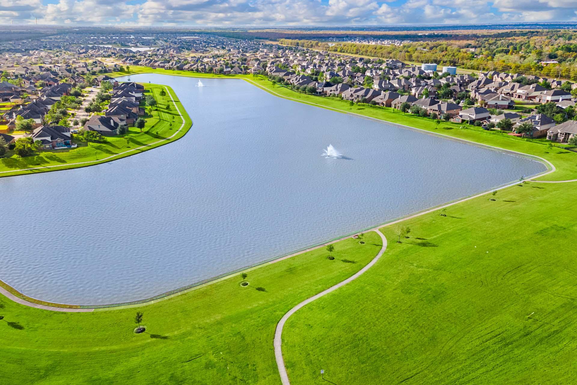 Aerial view of Sierra Vista neighborhood in Rosharon TX with curved lake, fountain, modern homes, and green walking paths by Davidson Homes