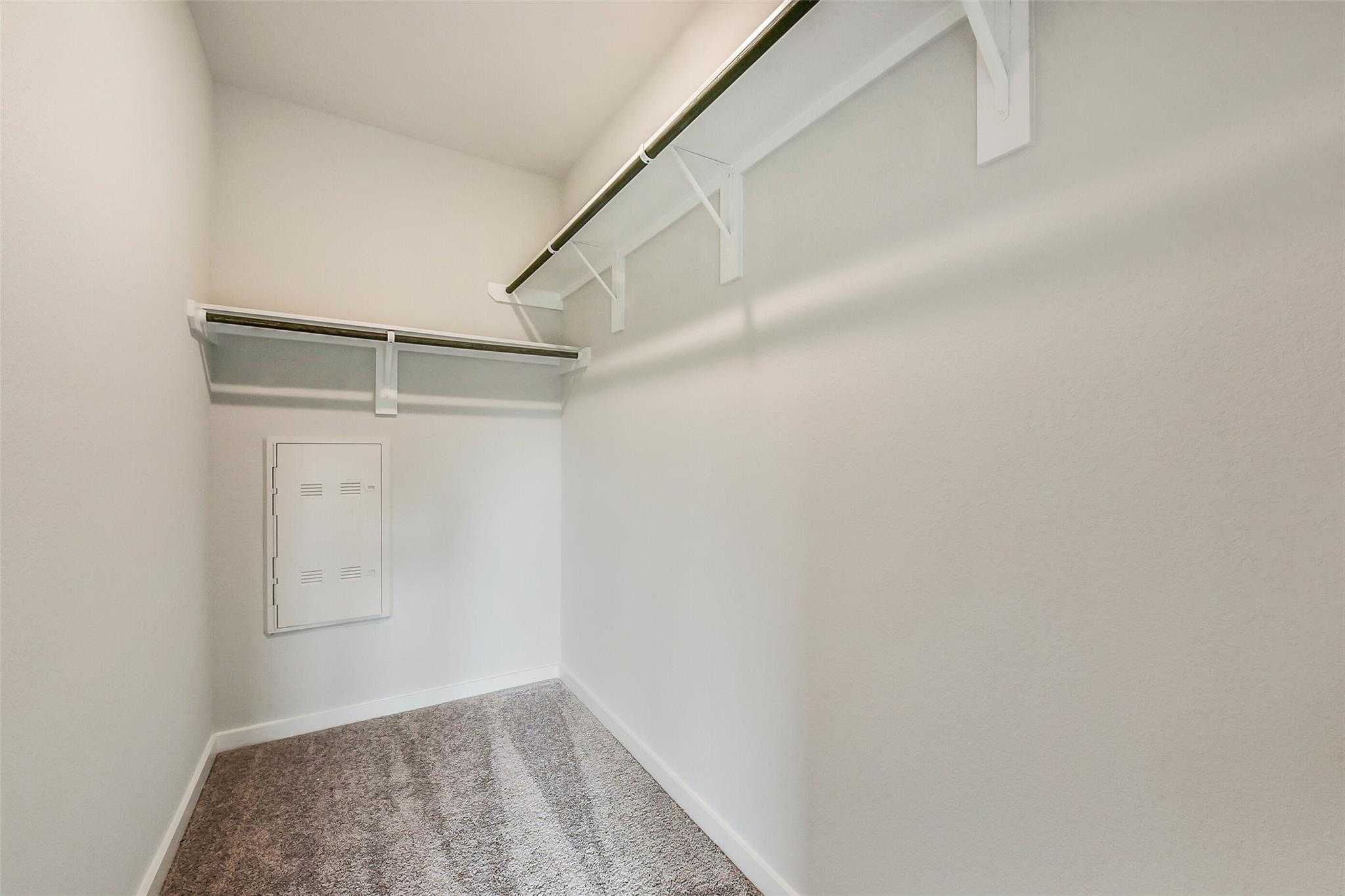 Spacious walk-in closet with built-in wooden shelves, double hanging rods, and neutral carpet in Davidson Homes The Frio G, Dayton, Texas