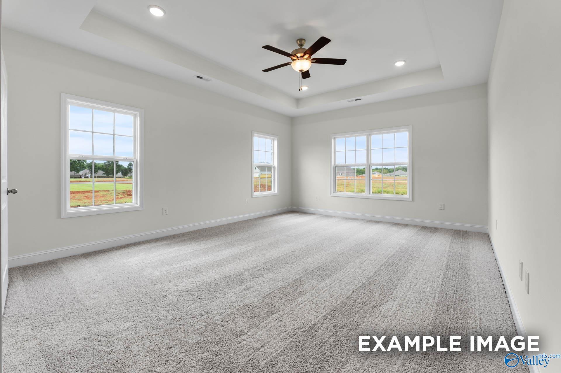 Spacious empty bedroom with gray carpet, large windows overlooking fields, tray ceiling fan in Davidson Homes The Emory, Toney, Alabama