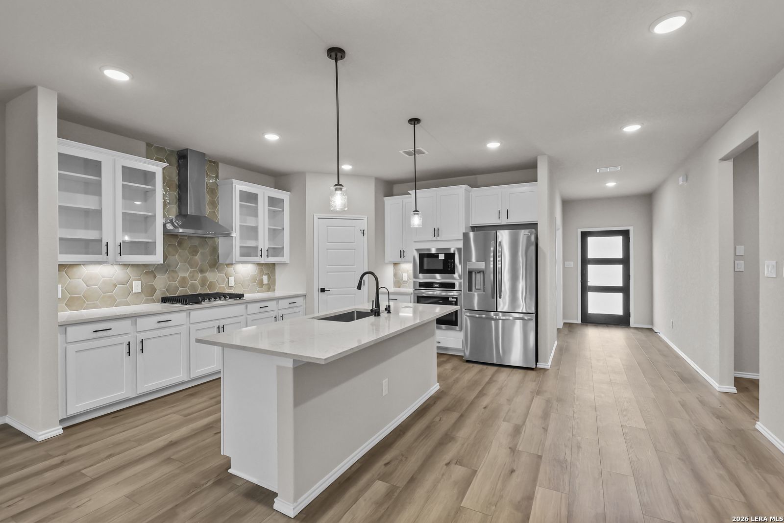 Modern white kitchen with island, stainless appliances, and hexagon tile backsplash in The Douglas F home in Bricewood.