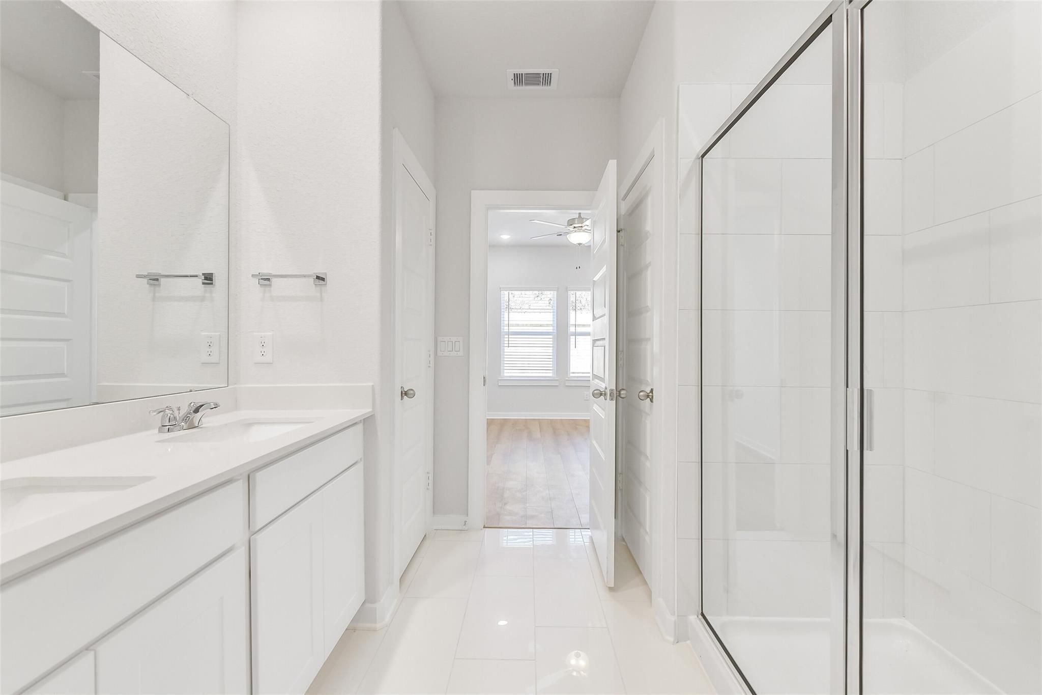 Bright primary bathroom with double vanity, frameless glass shower, white tile floors in Davidson Homes The Blanco E, Magnolia, Texas
