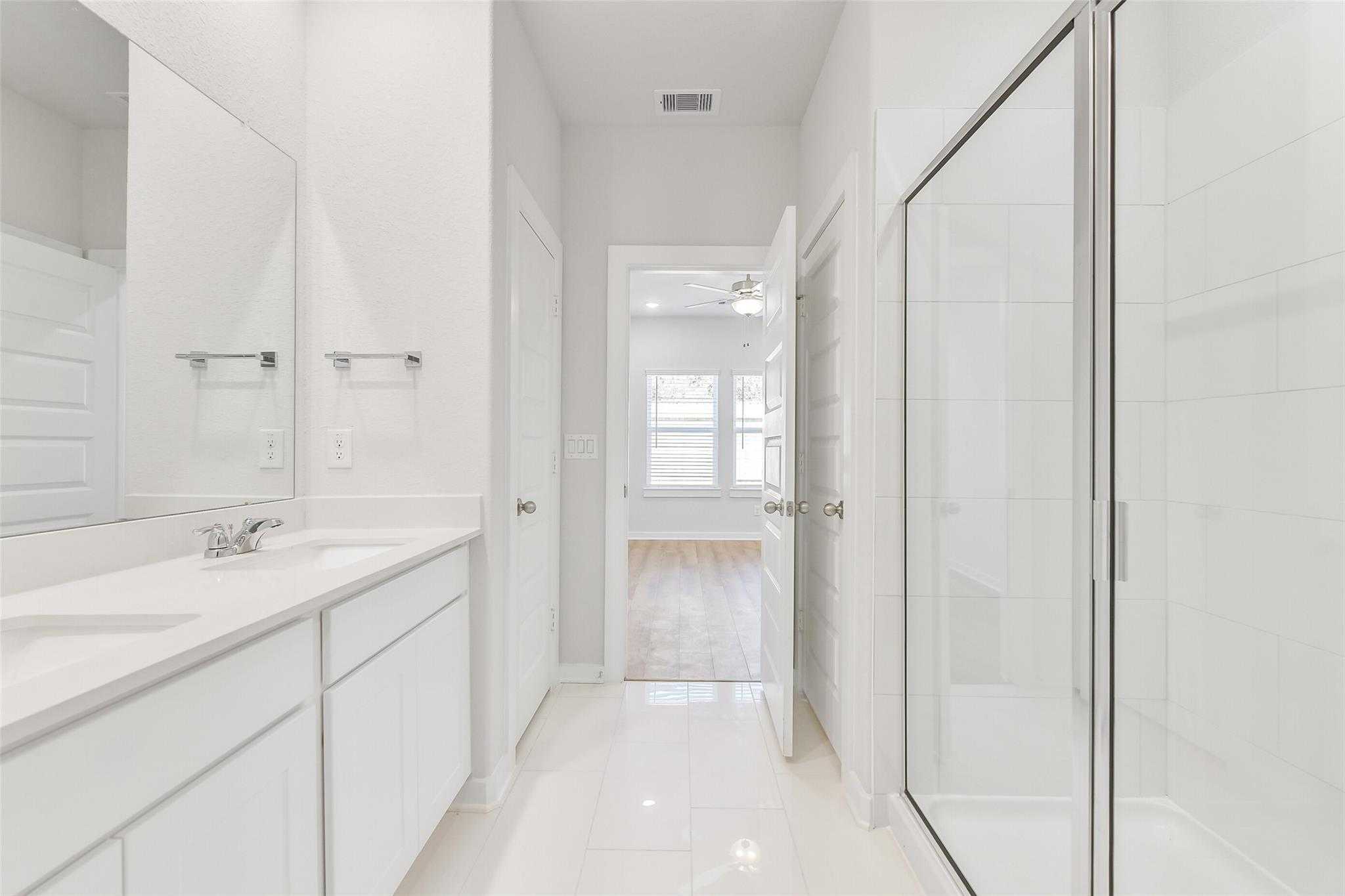 Bright primary bathroom with double vanity, frameless glass shower, white tile floors in Davidson Homes The Blanco E, Magnolia, Texas
