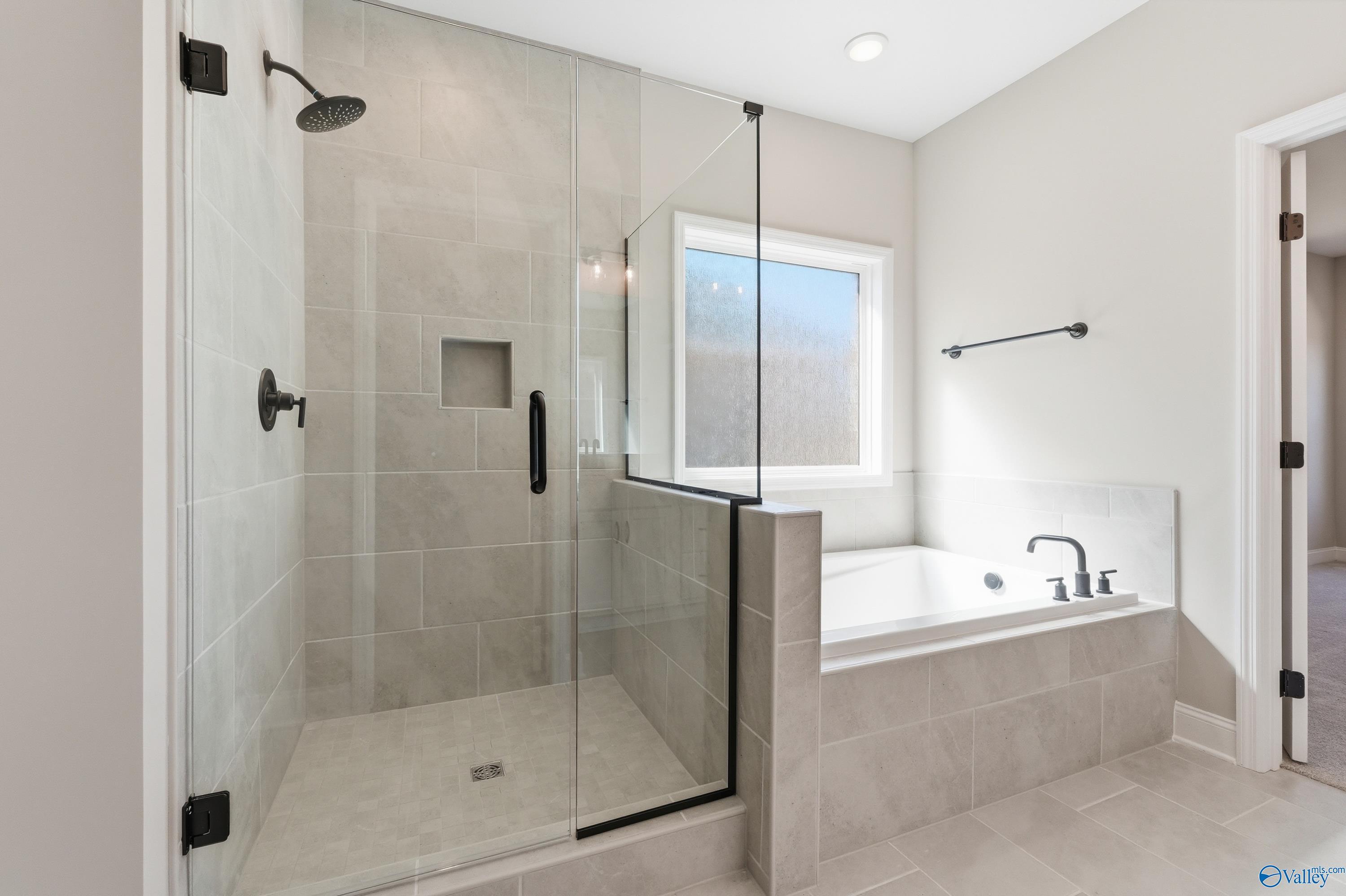 Modern master bathroom with frameless glass shower, soaking tub, and tiled accents in Davidson Homes The Rockford, Harvest AL