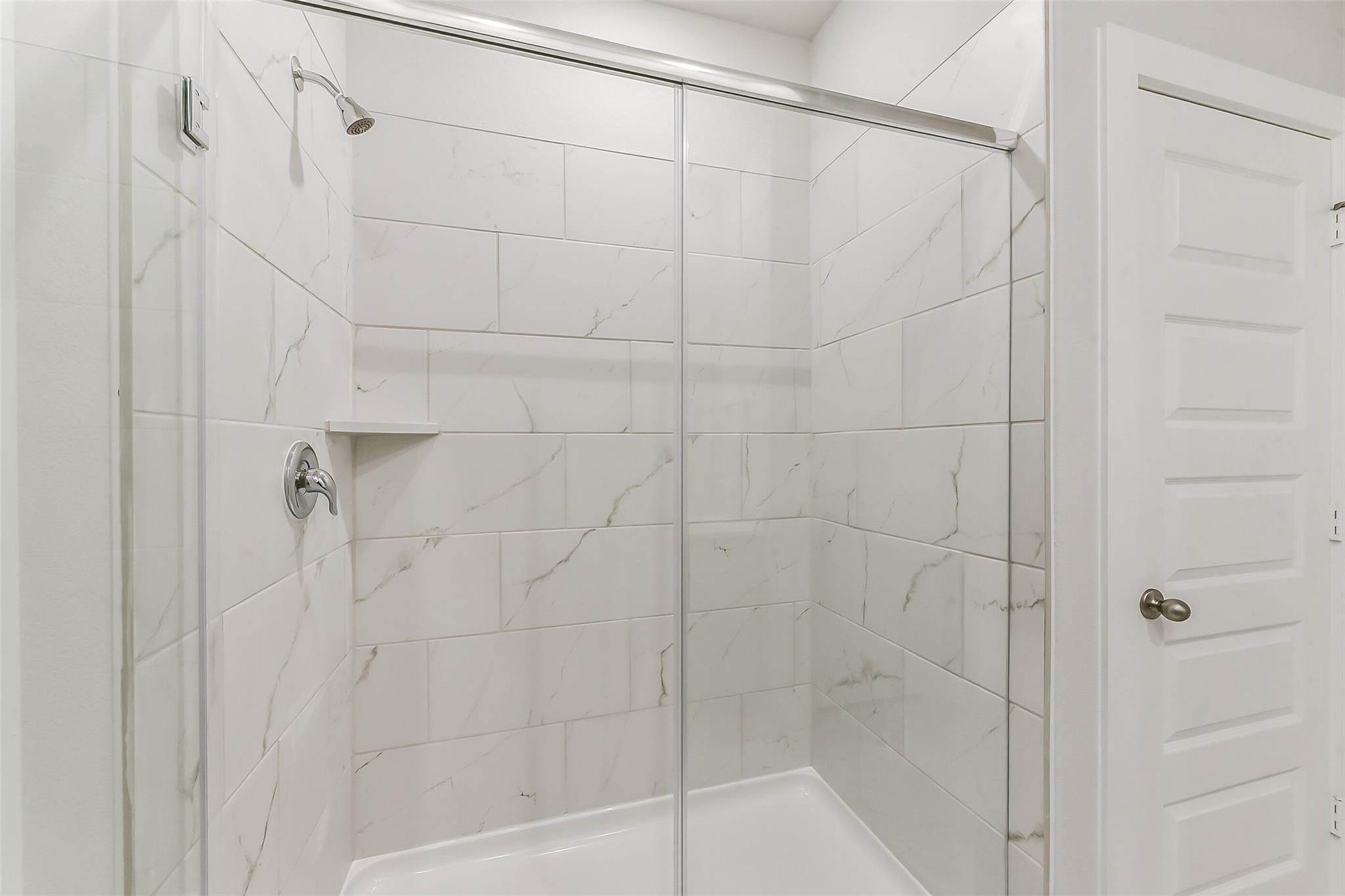 Modern glass shower enclosure with subway tile walls and niche shelf in master bathroom, Davidson Homes The Brazos E, Magnolia, Texas