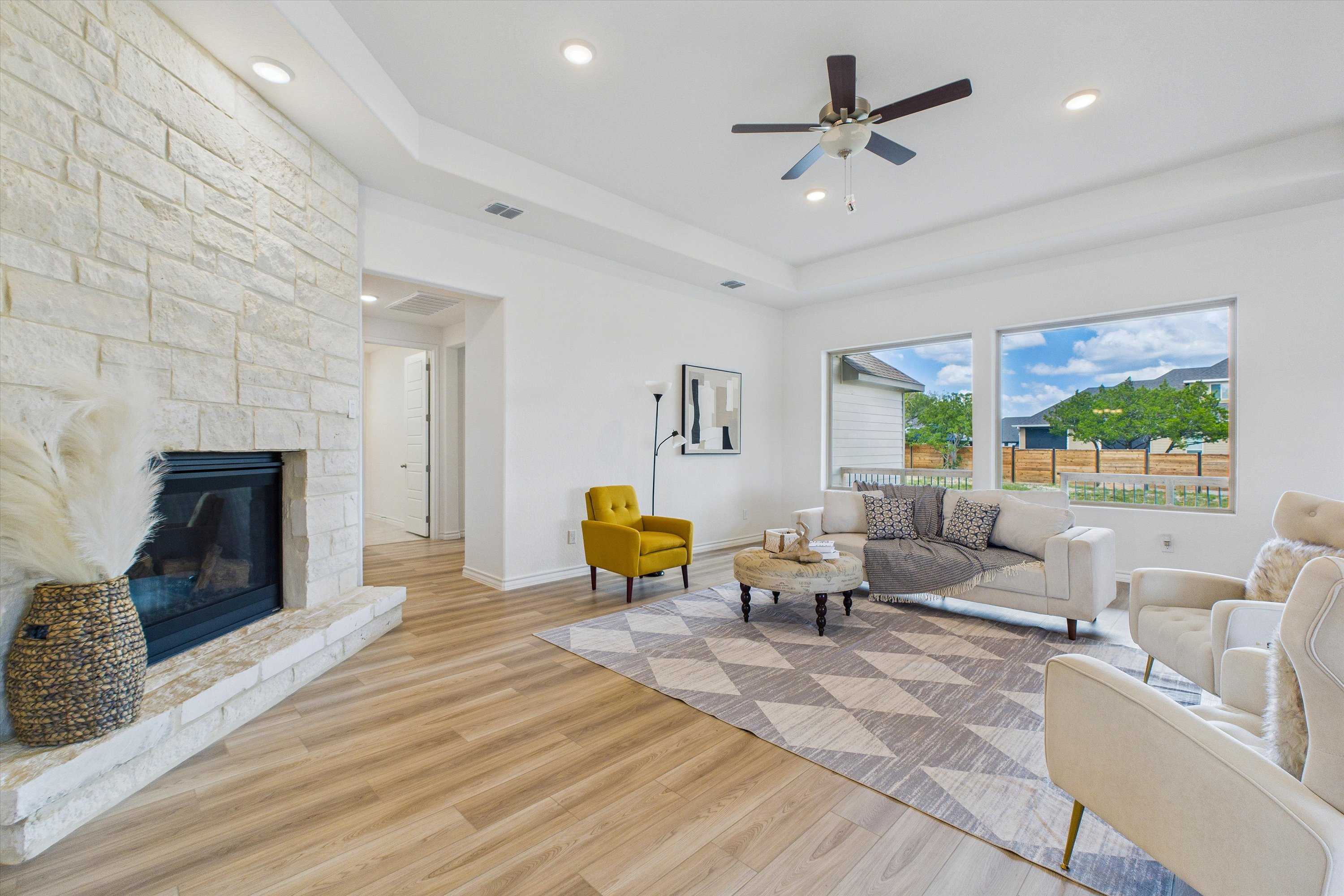 Cozy living room with stone fireplace, beige sectional sofa, yellow accent chair, and large windows in Davidson Homes The Summerlin C, Castroville, Texas