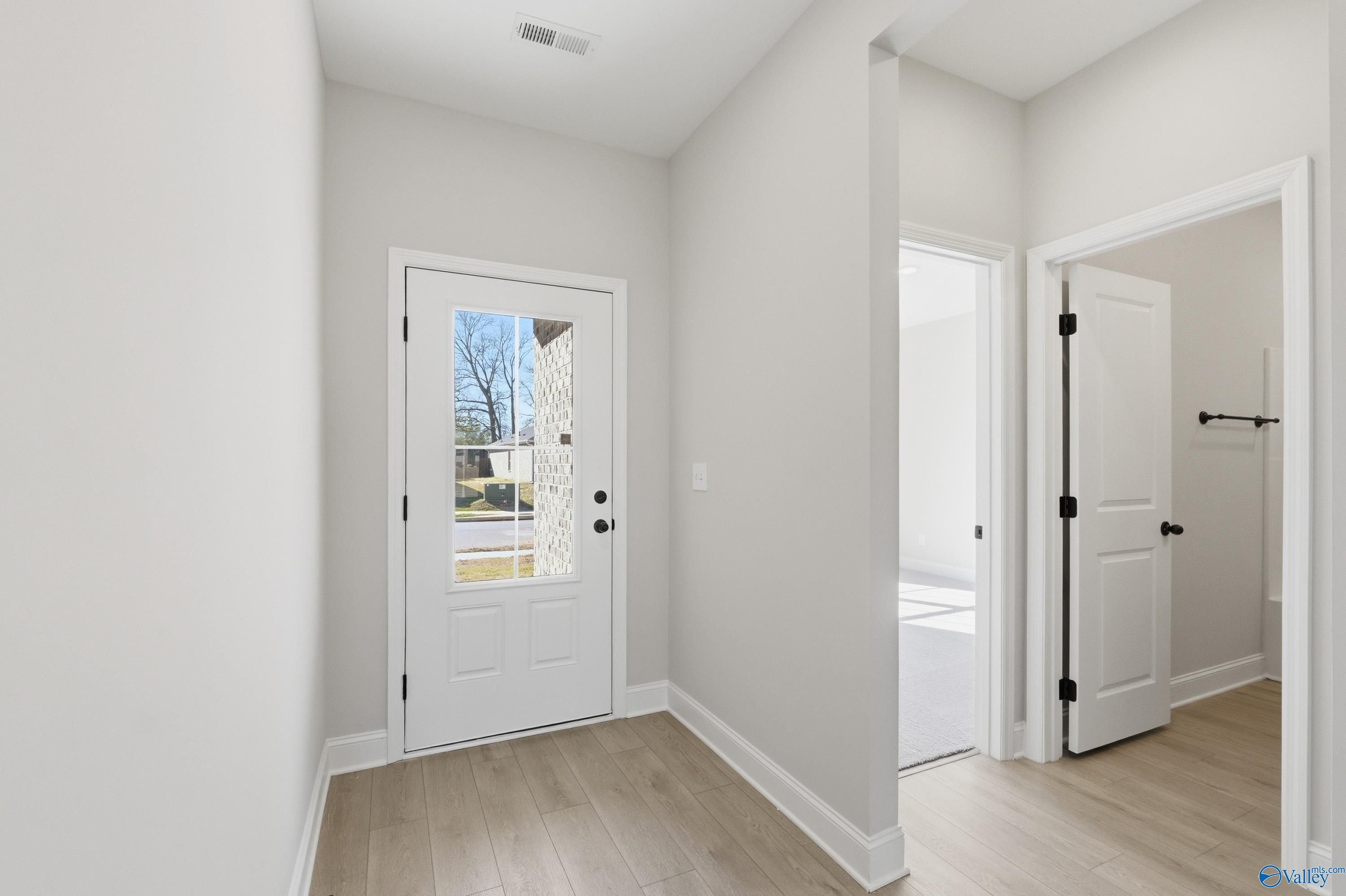 Bright entryway with glass-paneled front door, light wood floors, and open interior doors in The Franklin C 3-bedroom home, New Market, Alabama
