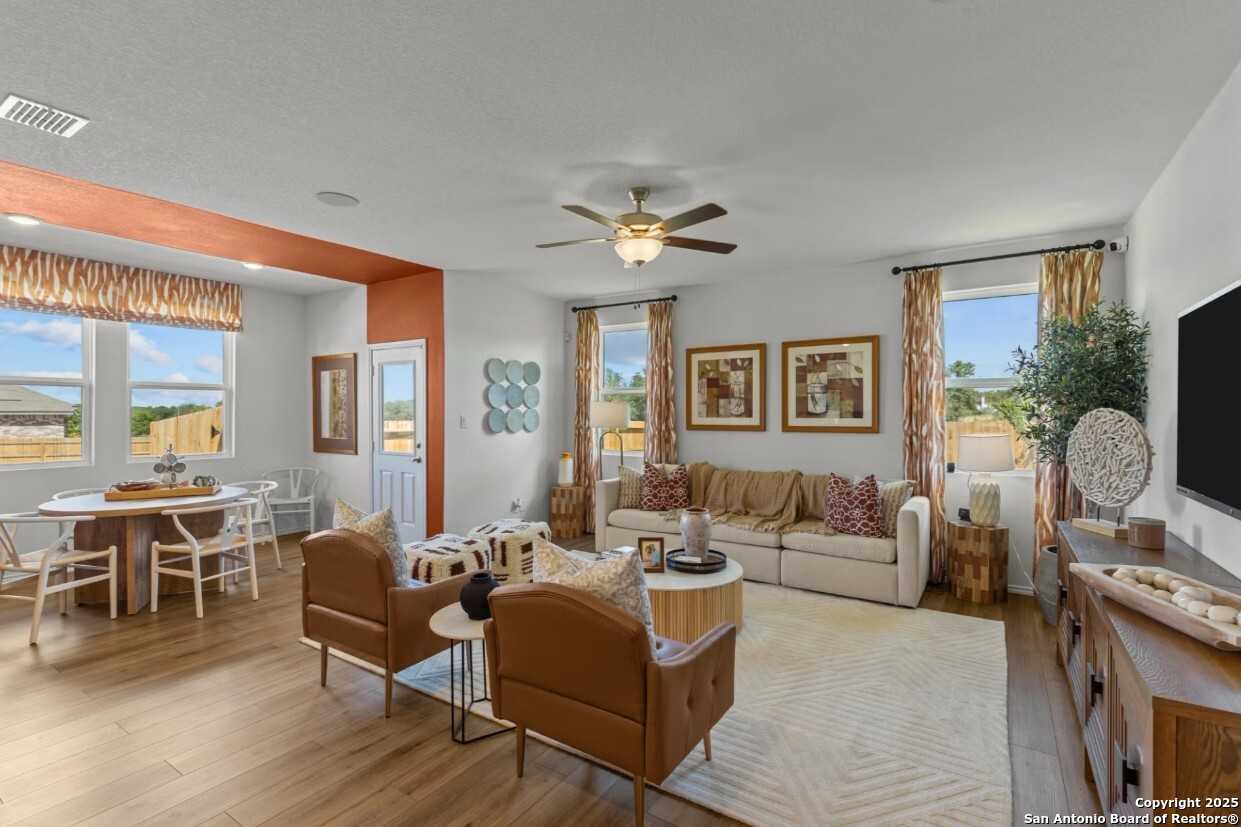 Spacious open-concept living room with beige sofa, wooden floors, dining table, and TV in Davidson Homes The Daphne J, Elmendorf, Texas