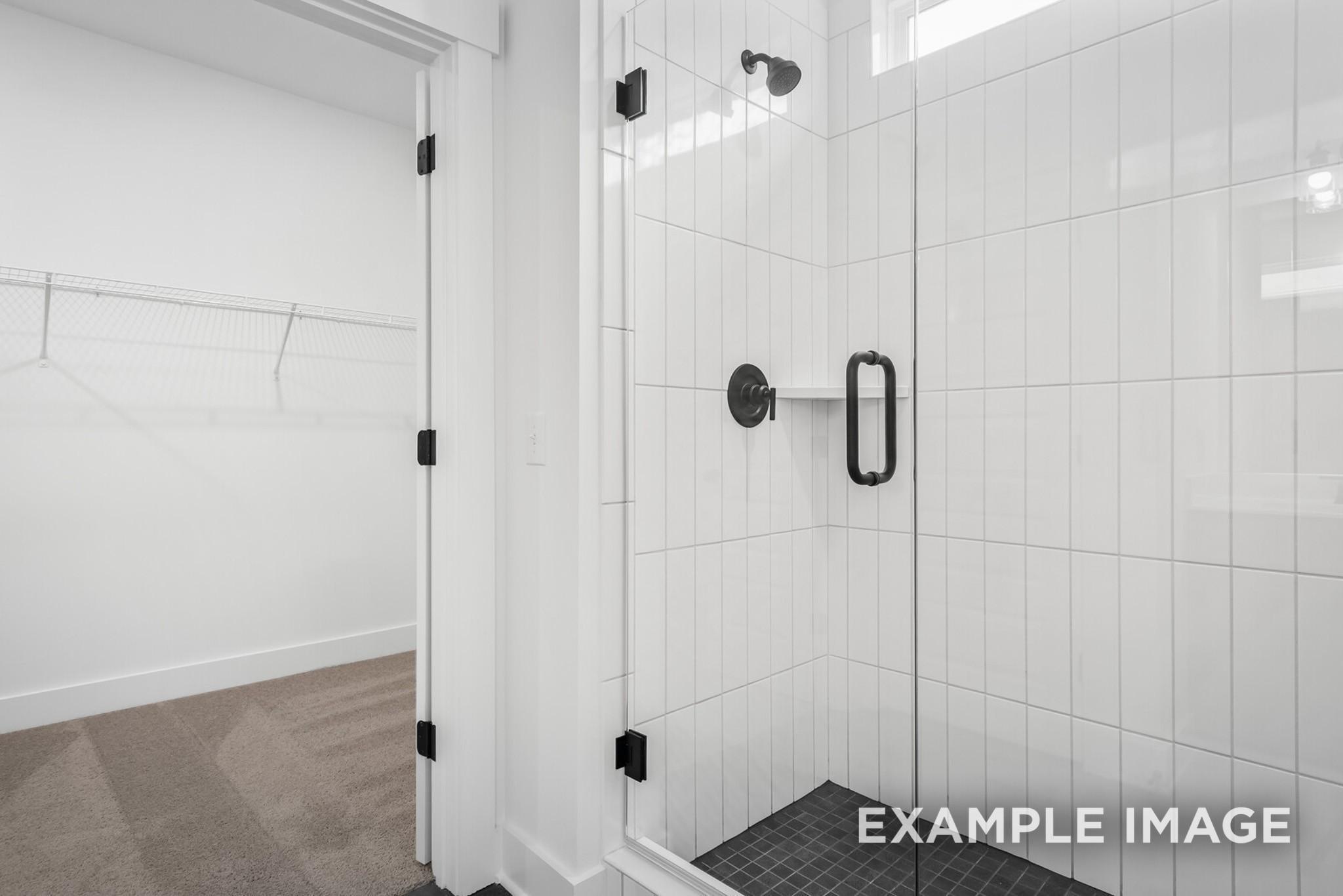 Modern white subway tile walk-in shower with glass door and bench, adjacent to walk-in closet in Davidson Homes Ridgeport C, Gallatin, TN