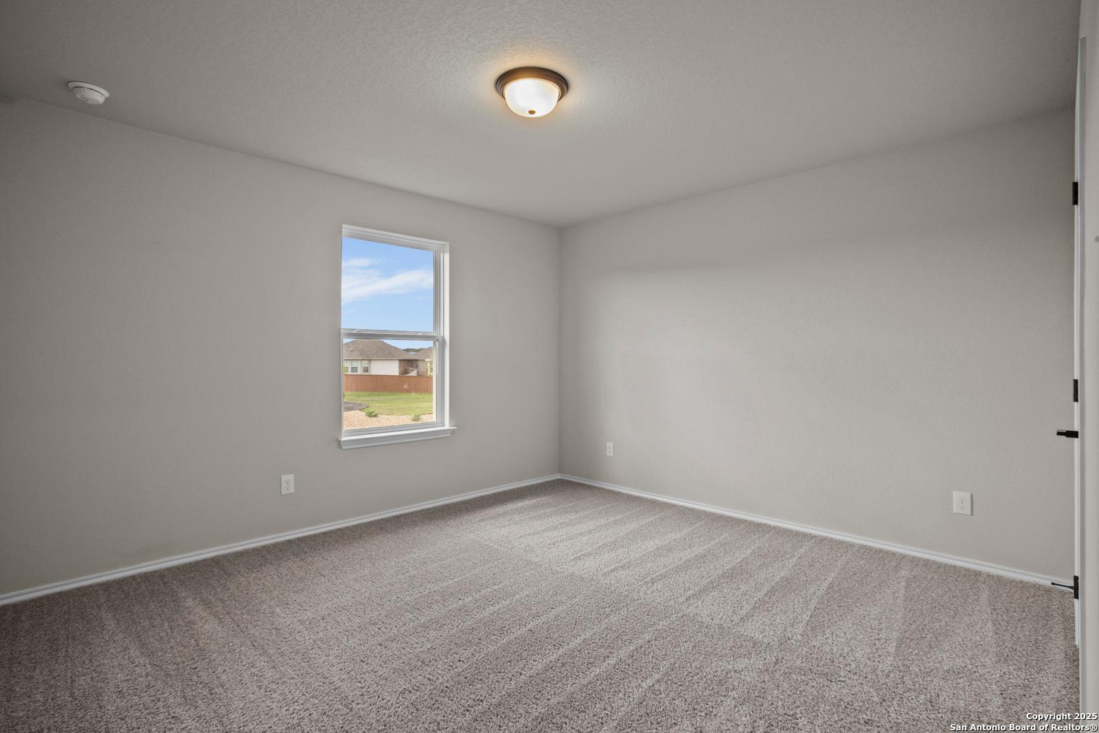 Empty secondary bedroom featuring light gray walls, plush carpet, and sunny window in Davidson Homes The Douglas F, Comanche Ridge, San Antonio