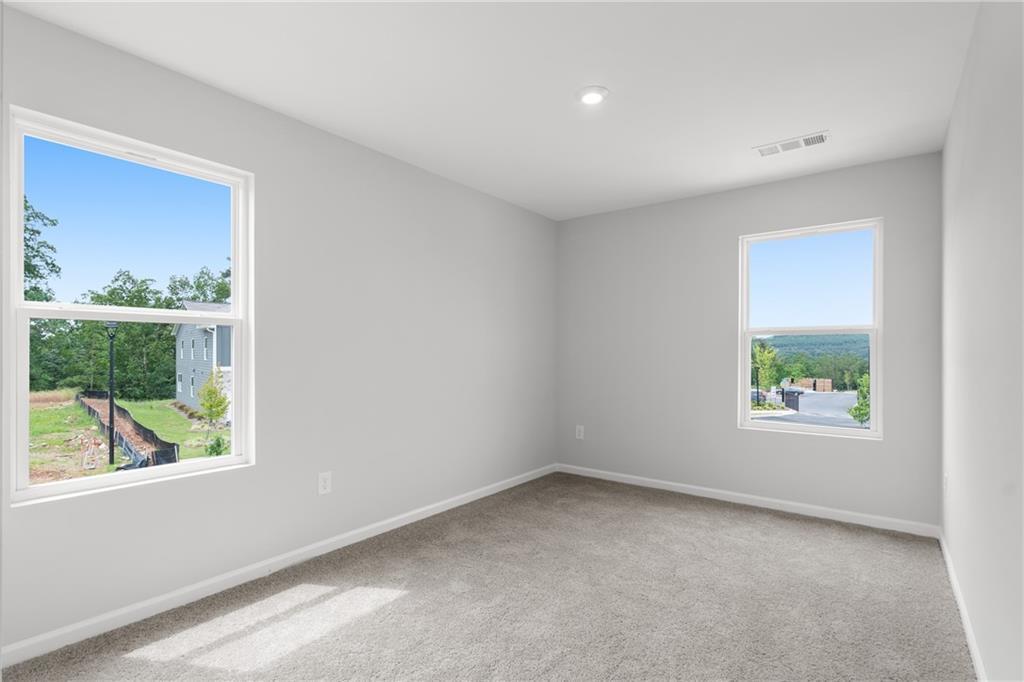 Bright secondary bedroom with gray walls, carpet, recessed lighting, and large windows overlooking wooded landscape in The Monroe B, Emerson, GA