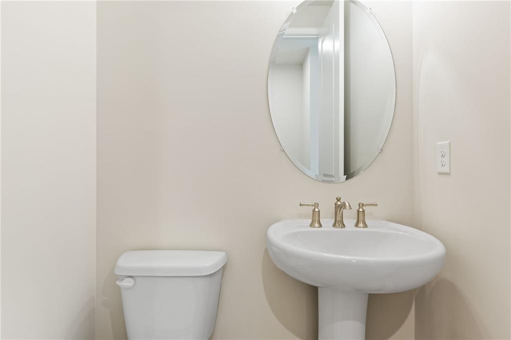 Elegant powder room with pedestal sink, round mirror, and toilet in Davidson Homes The Danbury C, Buford, Georgia