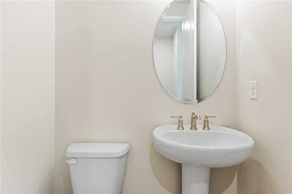 Elegant powder room featuring pedestal sink, gold faucets, round mirror in The Hampton C by Davidson Homes, Buford, Georgia