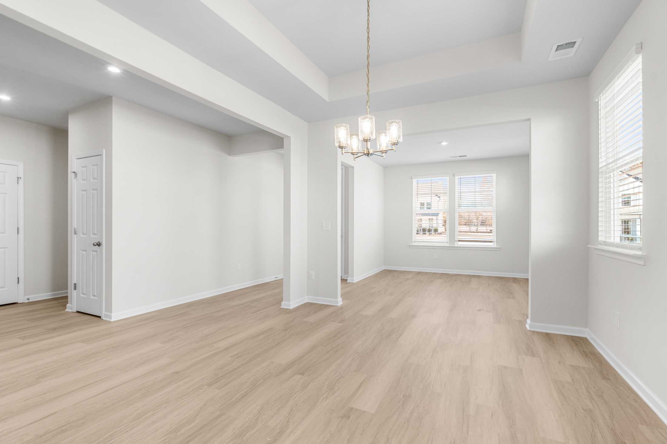 Spacious open-concept living room in The Glenwood A with hardwood floors, chandelier, and arched entries
