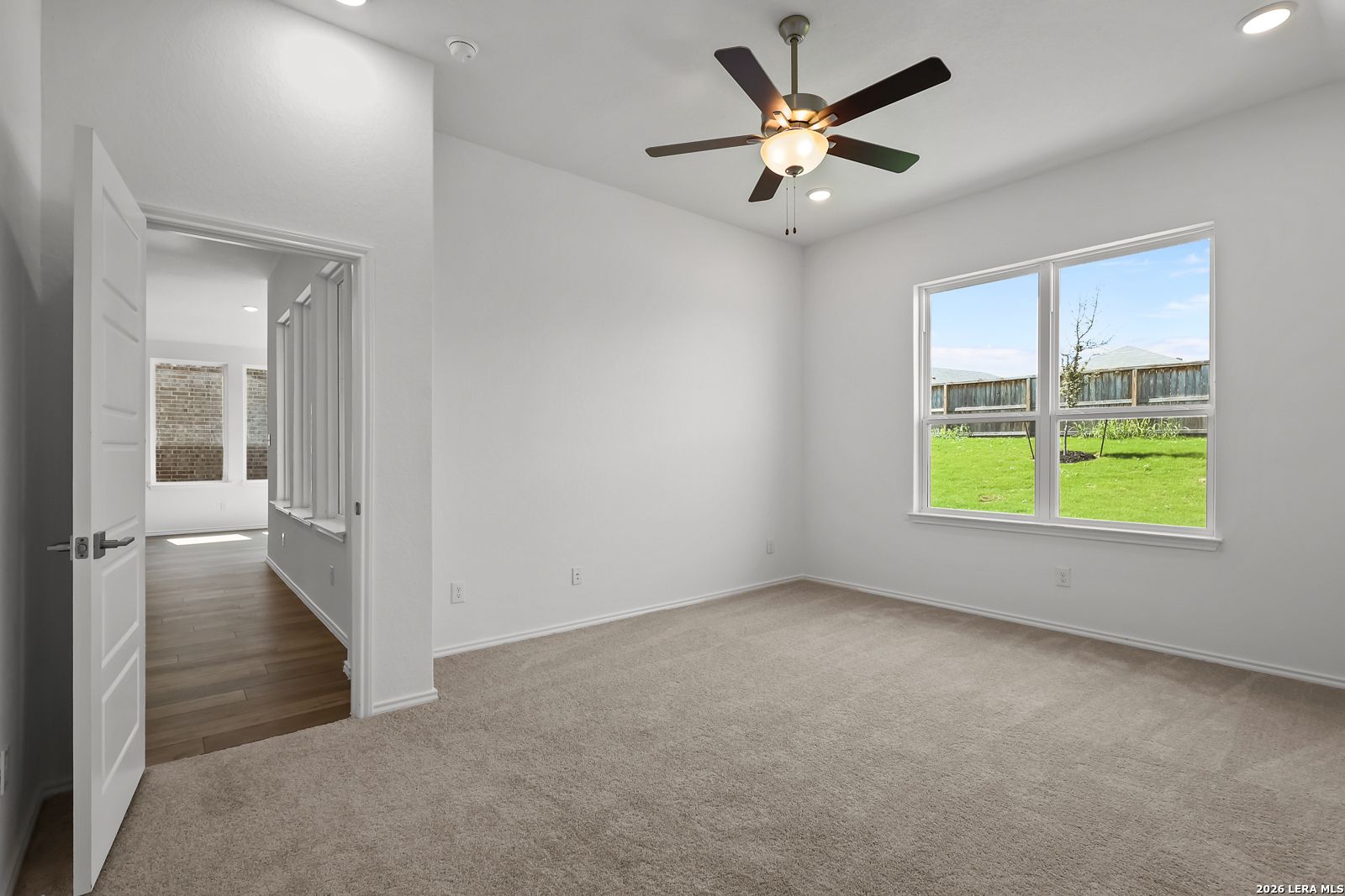 Bright bedroom with beige carpet, ceiling fan, and large windows overlooking lush green lawn in Davidson Homes The Sequoia B, San Antonio
