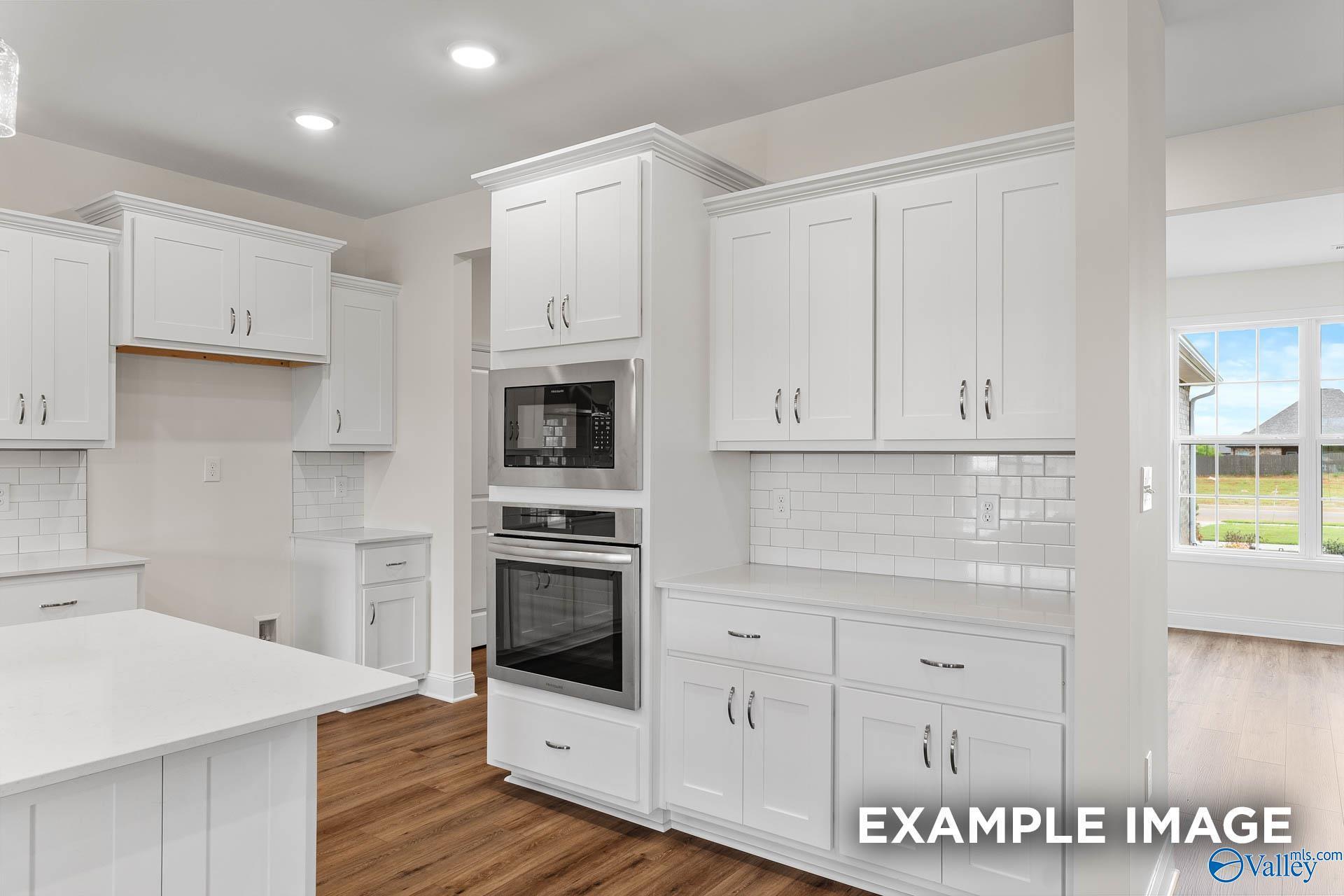 Bright white kitchen with island, double ovens, subway tile backsplash, and backyard view in The Emory 4-bedroom home, Toney, Alabama