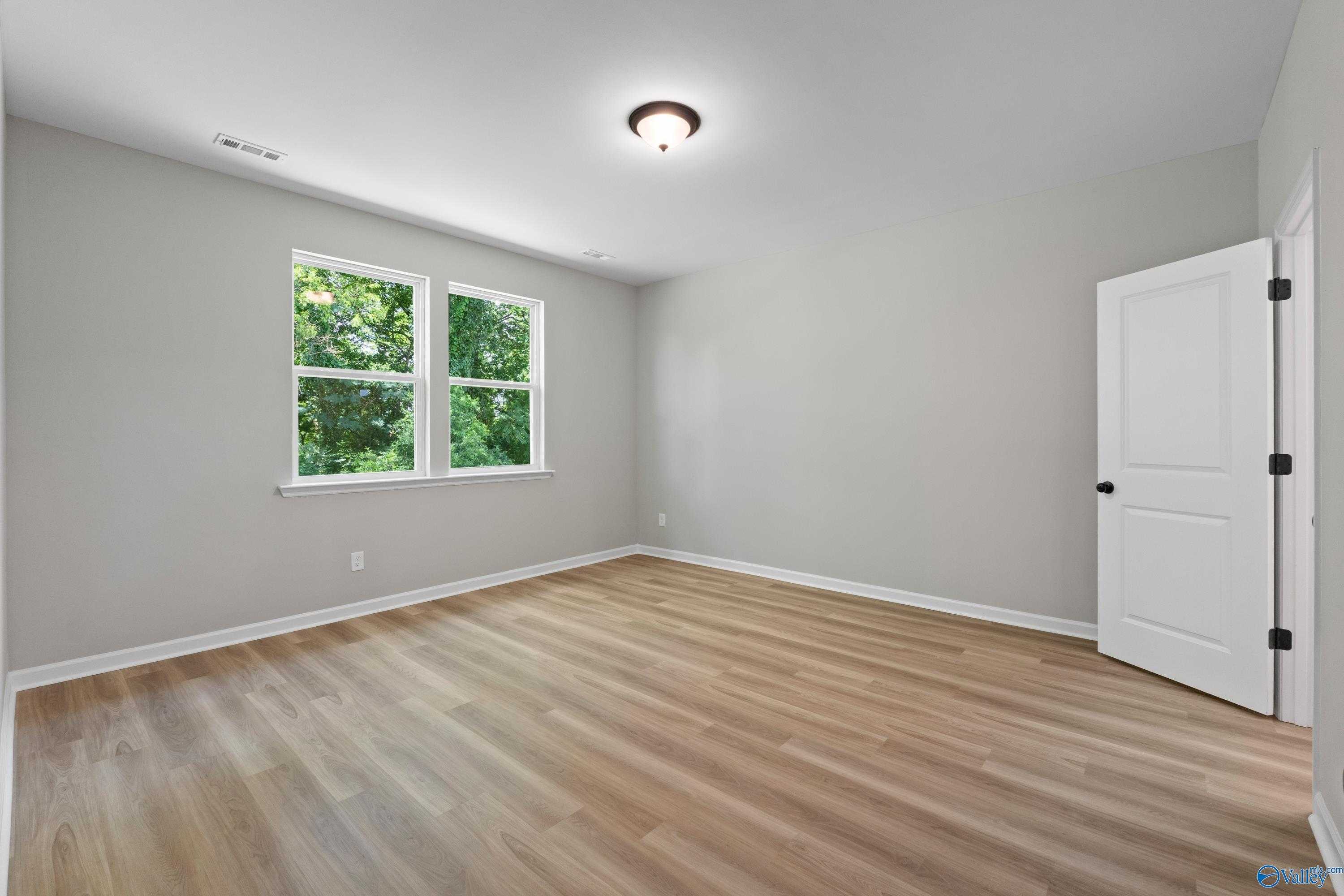 Bright bedroom with gray walls, large double windows overlooking trees, light laminate flooring in Davidson Homes The Phoenix, Hazel Green, AL