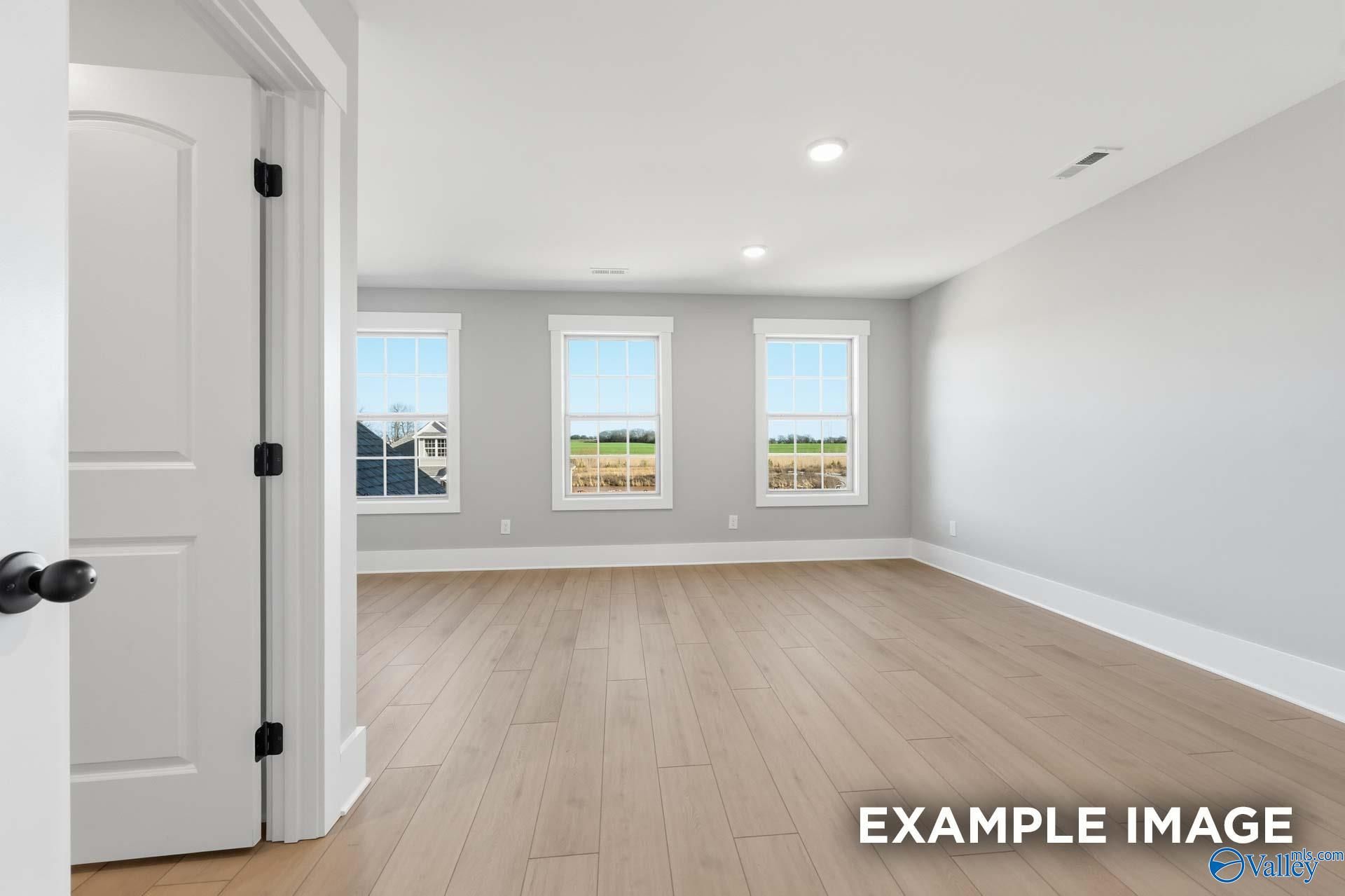 Spacious empty living room with hardwood floors, gray walls, and large windows overlooking green fields in Davidson Homes The Emory, Decatur, Alabama