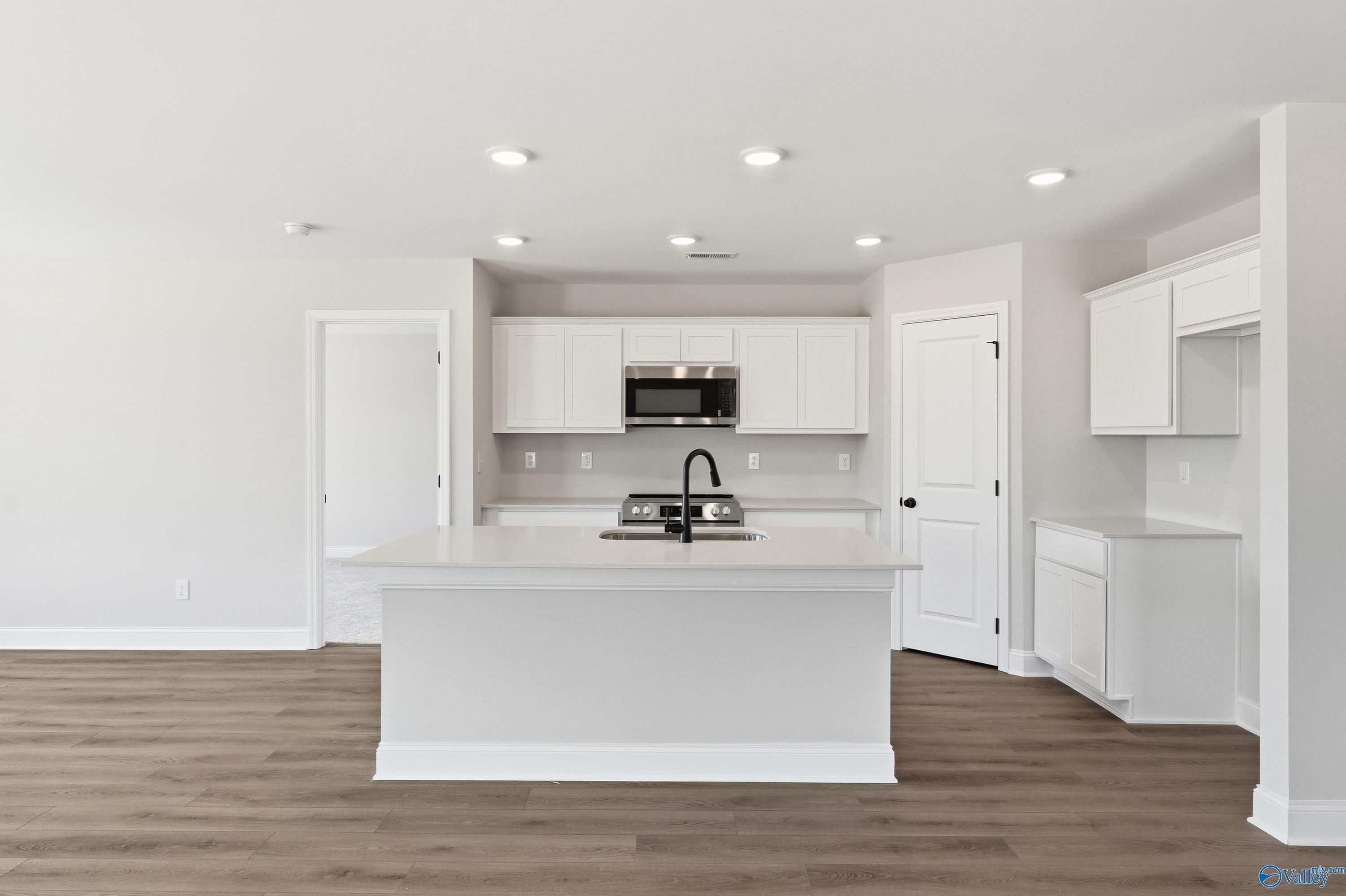 Modern white kitchen with large island, stainless appliances, and recessed lights in The Franklin V home, Athens, Alabama