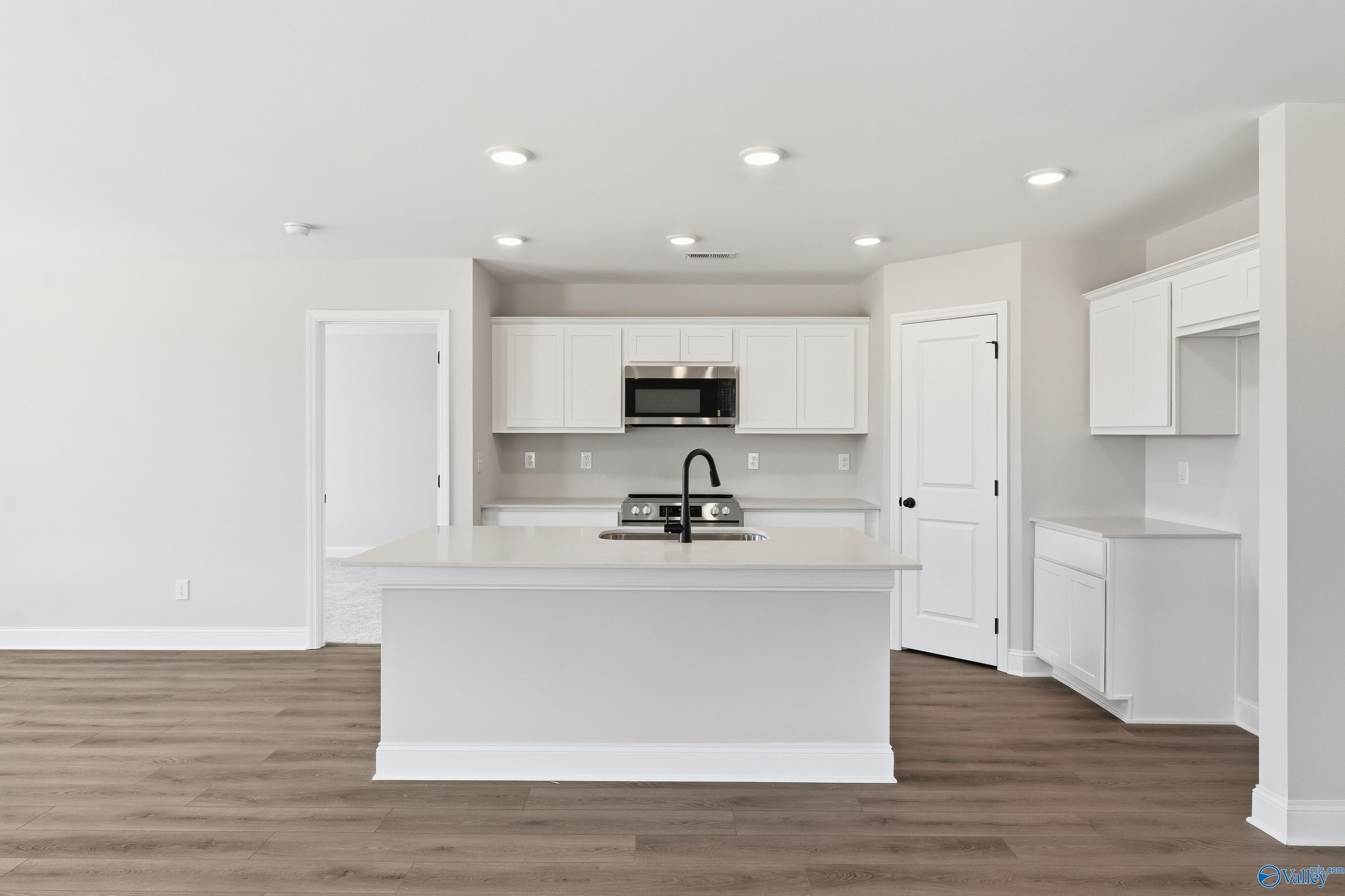 Modern white kitchen with large island, stainless appliances, and recessed lights in The Franklin V home, Athens, Alabama