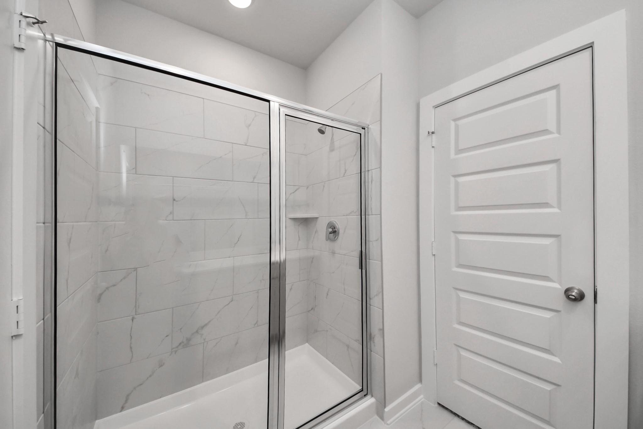 Modern glass walk-in shower with white marble tile in bathroom of Davidson Homes The Frio F plan, Robins Landing Houston