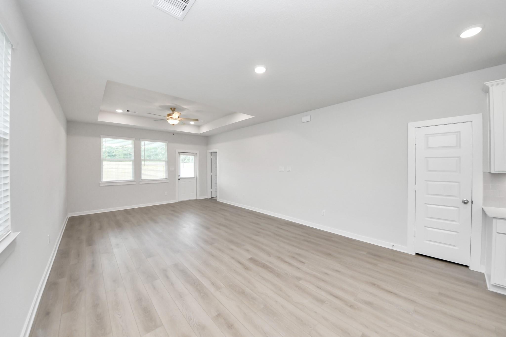 Spacious open-concept living area with tray ceiling and wood-style flooring in The Frio F home at Liberty Estates, Texas.