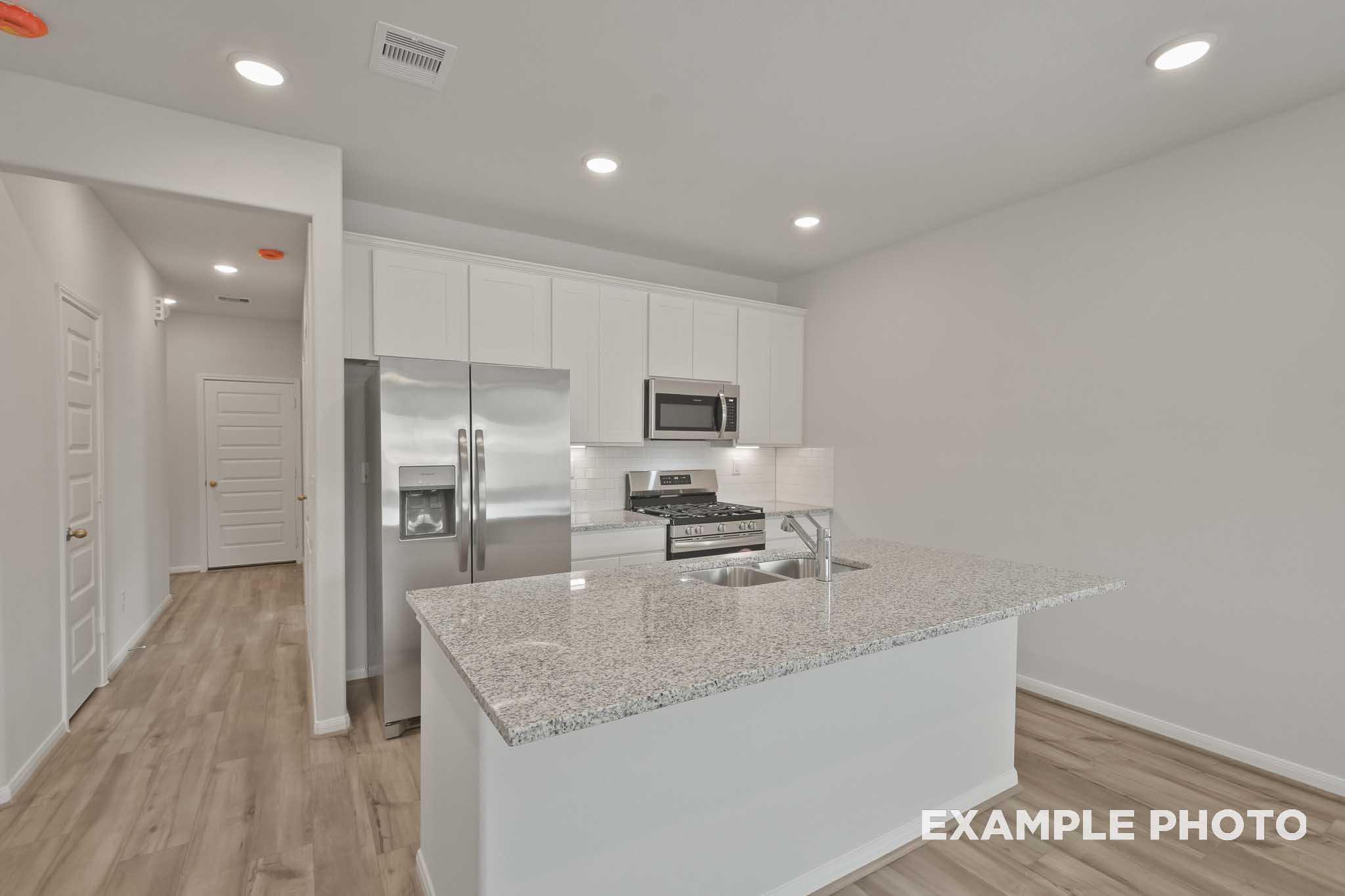 Spacious kitchen in The Comal with white shaker cabinets, stainless steel appliances, granite island, and open layout