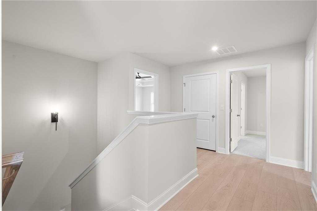 Bright upstairs hallway with light oak floors, white walls, railings, and doors in The Hickory B home, Buford, GA