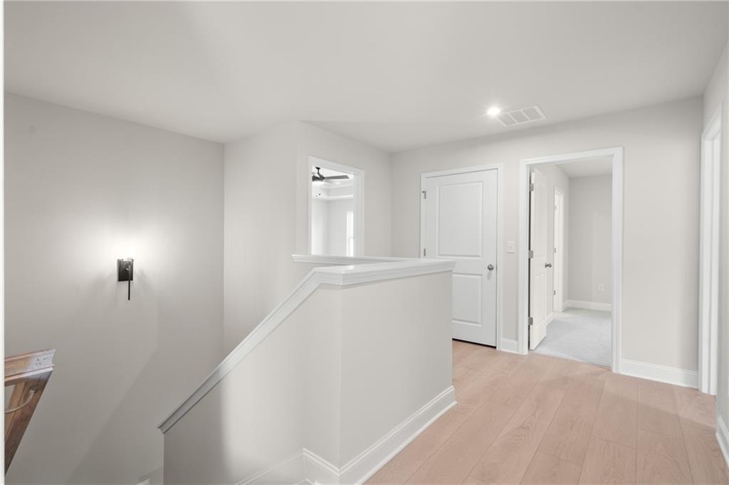 Bright upstairs hallway with oak hardwood floors, white walls, doors, and staircase railing in Davidson Homes The Hickory E, Buford, Georgia