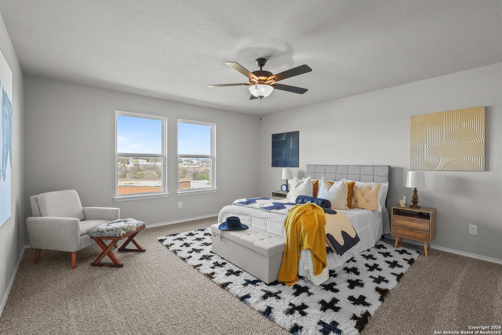 Cozy master bedroom with gray headboard bed, ceiling fan, large windows, and accent chair in Davidson Homes The Murray K, San Antonio