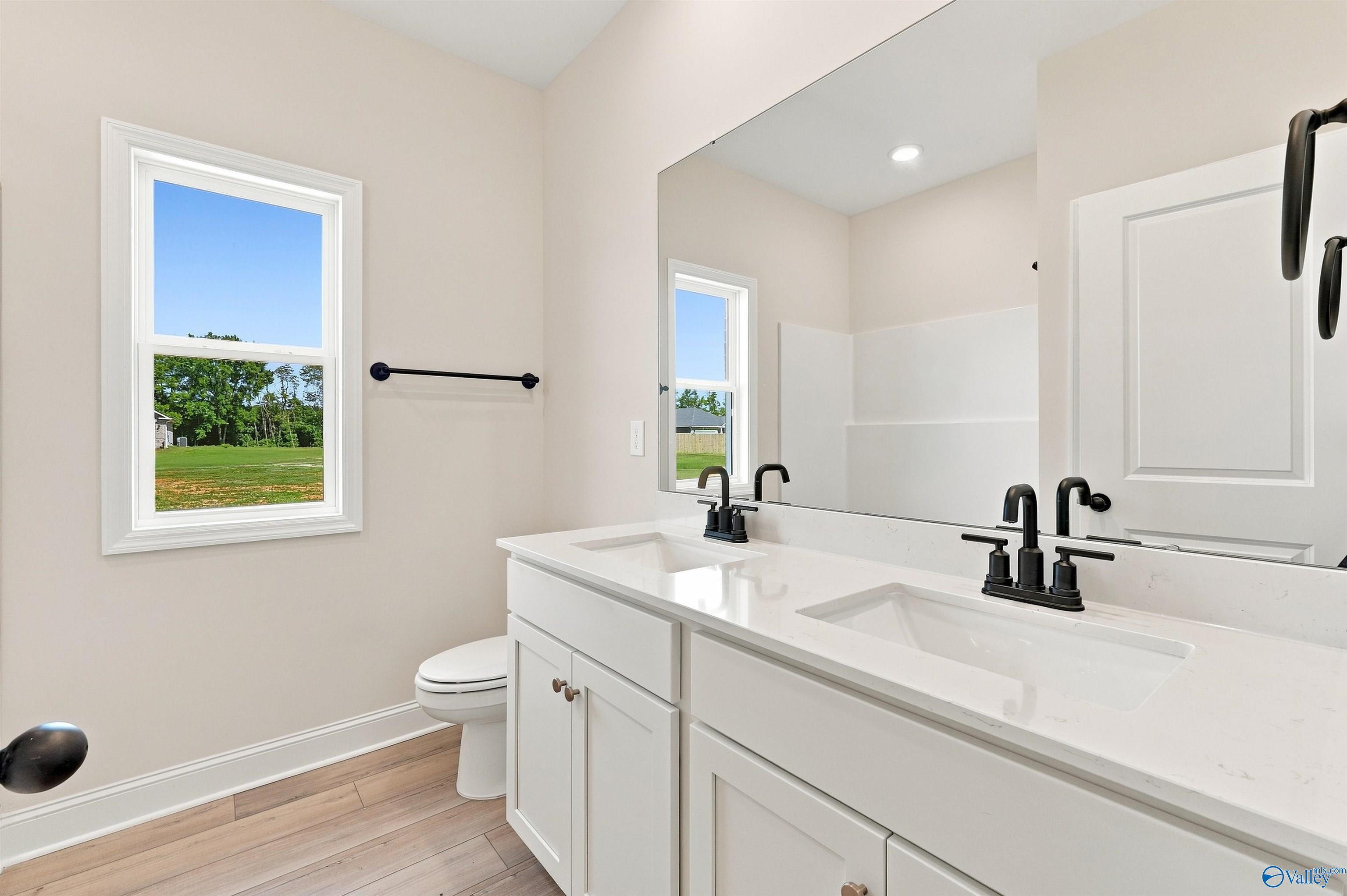 Bright bathroom with double vanity, white quartz countertops, matte black faucets, and wood-look flooring in Davidson Homes The Everett B, Toney Alabama