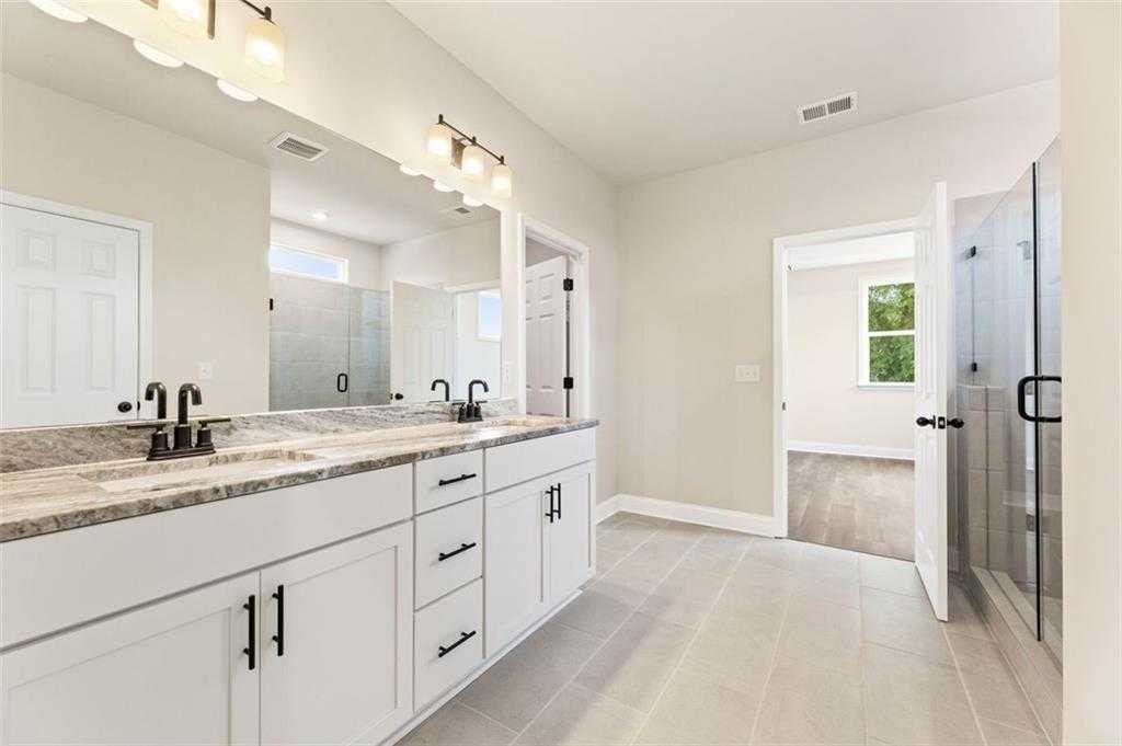 Modern master bathroom featuring double vanity with quartz counters, white cabinets, and frameless glass shower in Davidson Homes The Harrison G, Hoschton, GA