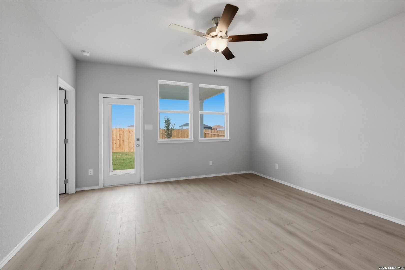 Bright living room with gray walls, laminate wood floors, ceiling fan, and large windows to fenced backyard in Davidson Homes The Frio B, Agave San Antonio Texas